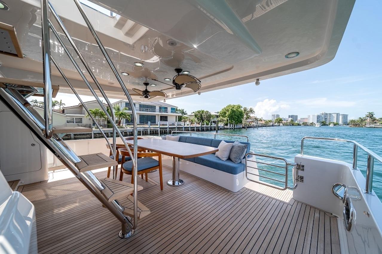 Luxurious 2027 Offshore Yachts 70 CE deck with seating, table, and waterfront view.