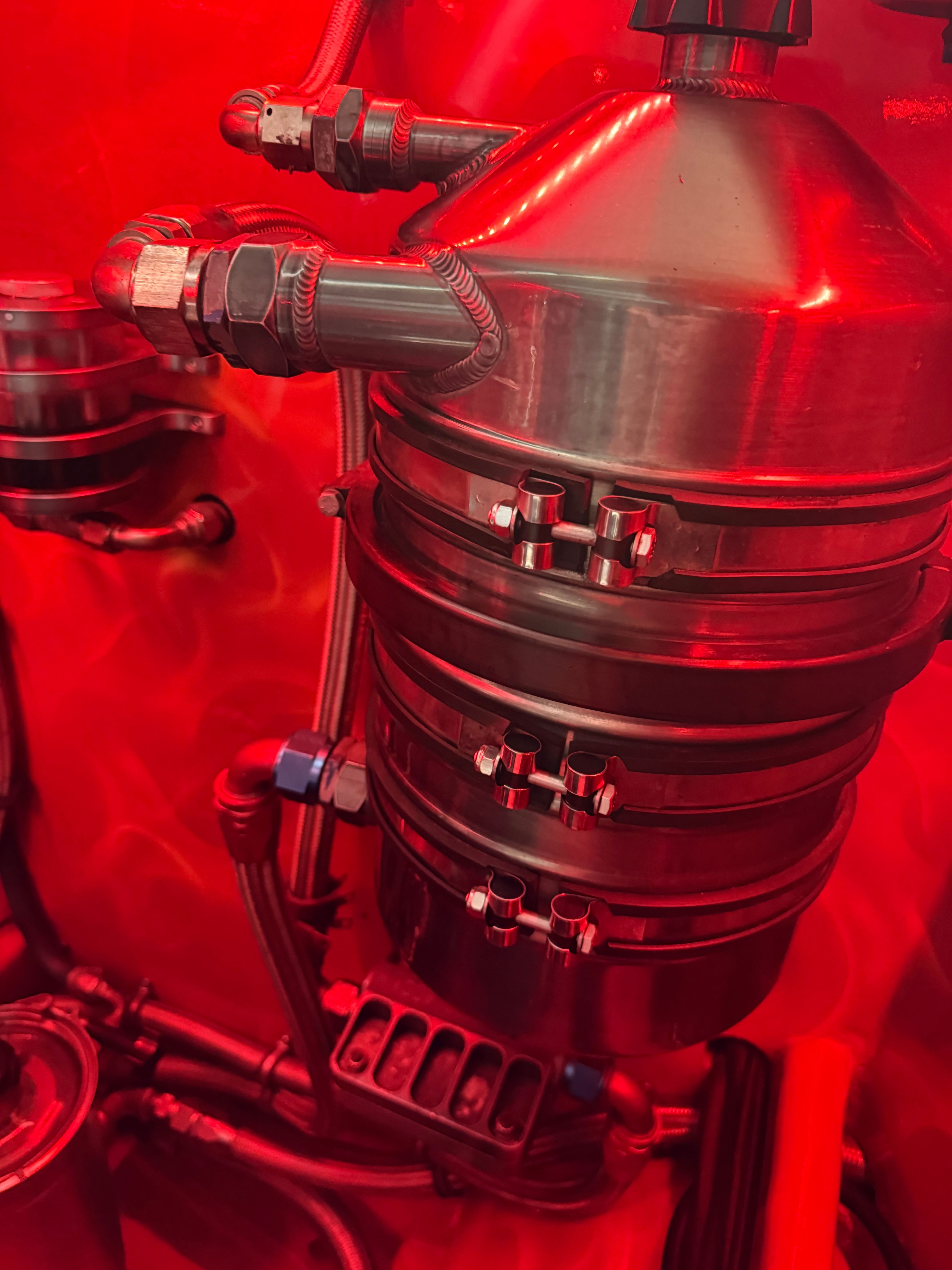 Close-up of a shiny metal engine part with hoses and fittings, illuminated in red.