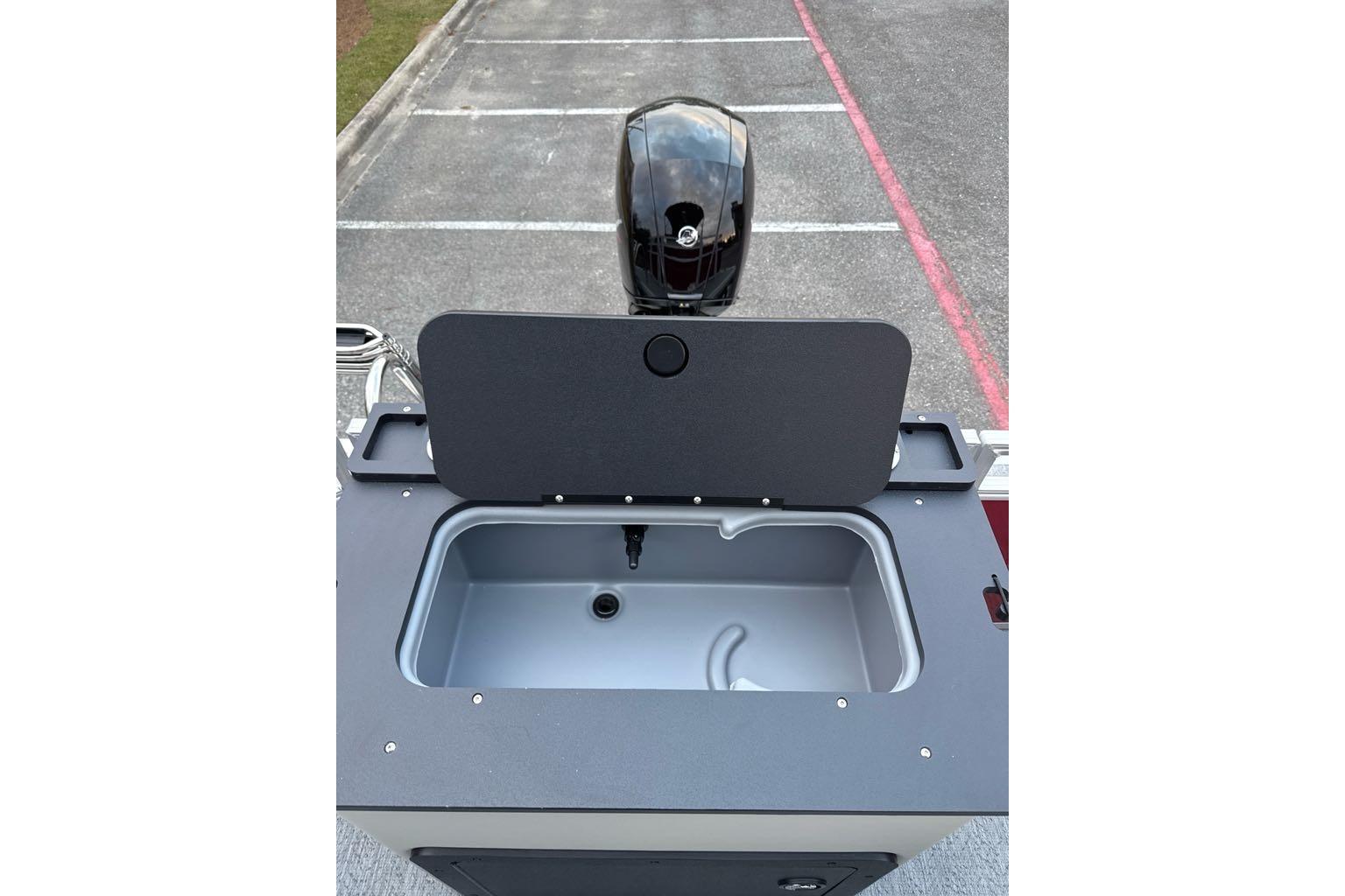 2026 Sun Tracker Fishin' Barge 22 DLX livewell and motor in parking lot.