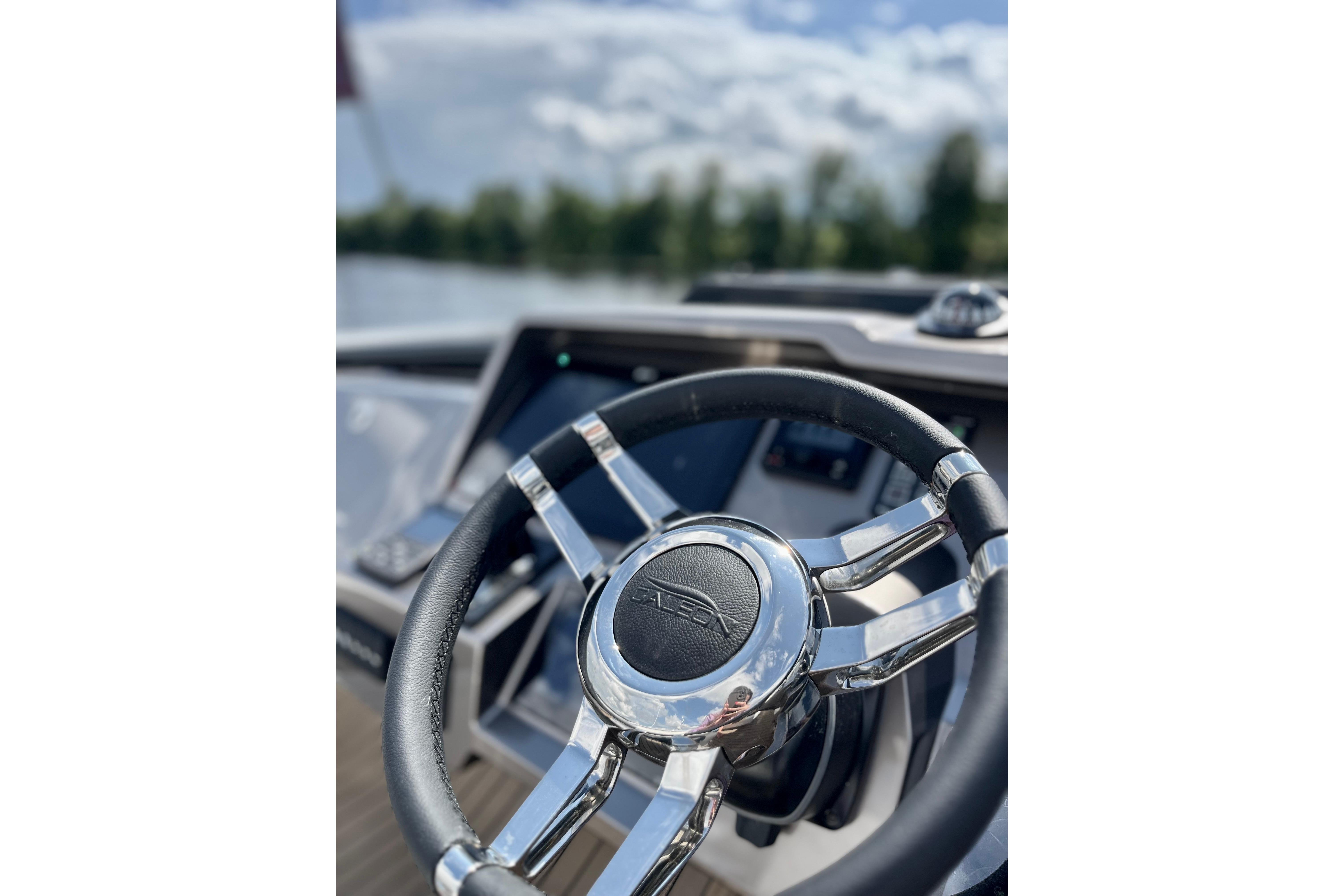 Steering wheel of 2025 Galeon 700 Sky yacht, with blurred water and sky background.