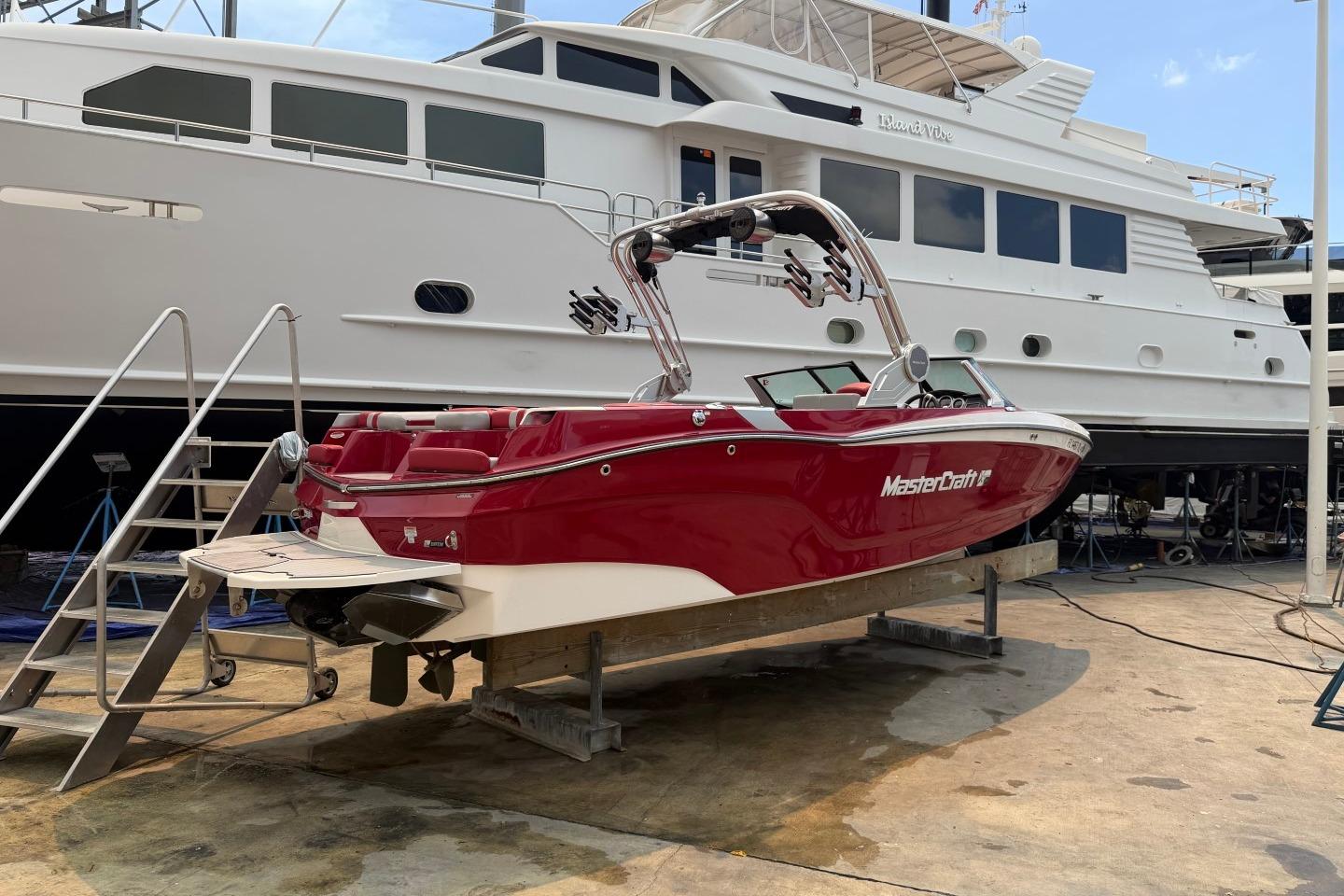 2023 MasterCraft X24 boat in red, docked beside a large yacht.