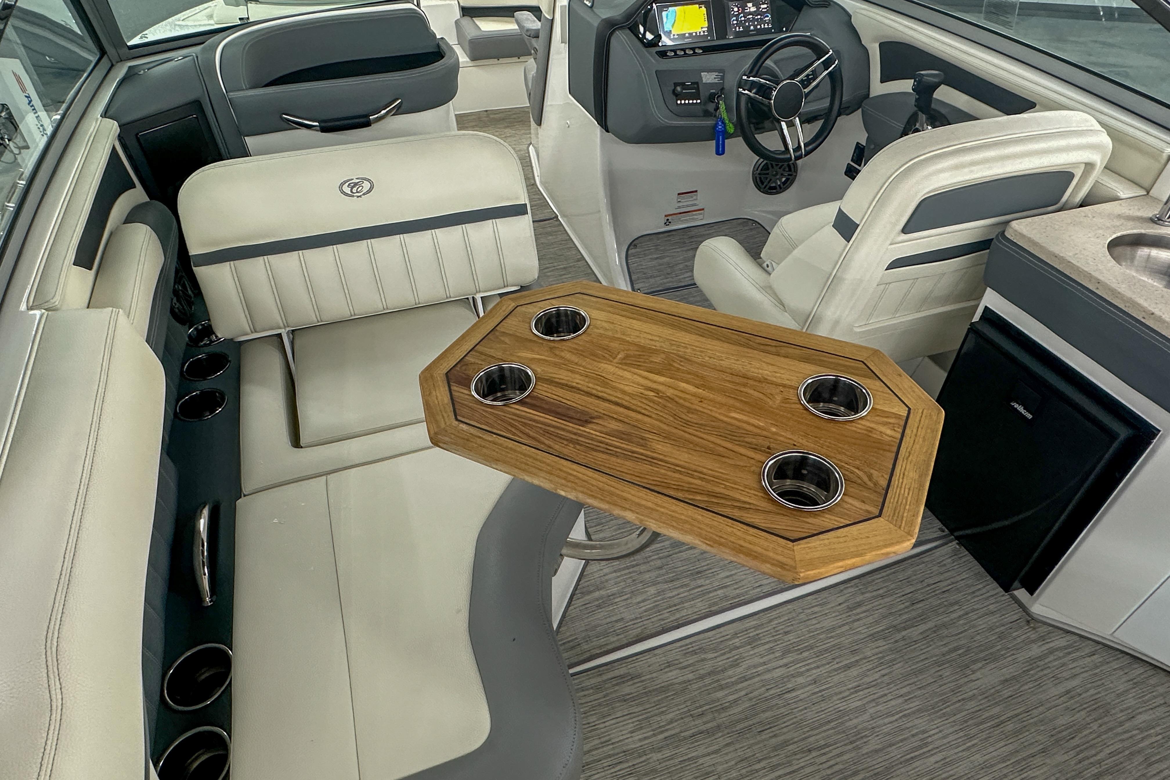 Interior of 2022 Cobalt 25SC boat with seating, wooden table, and steering console.