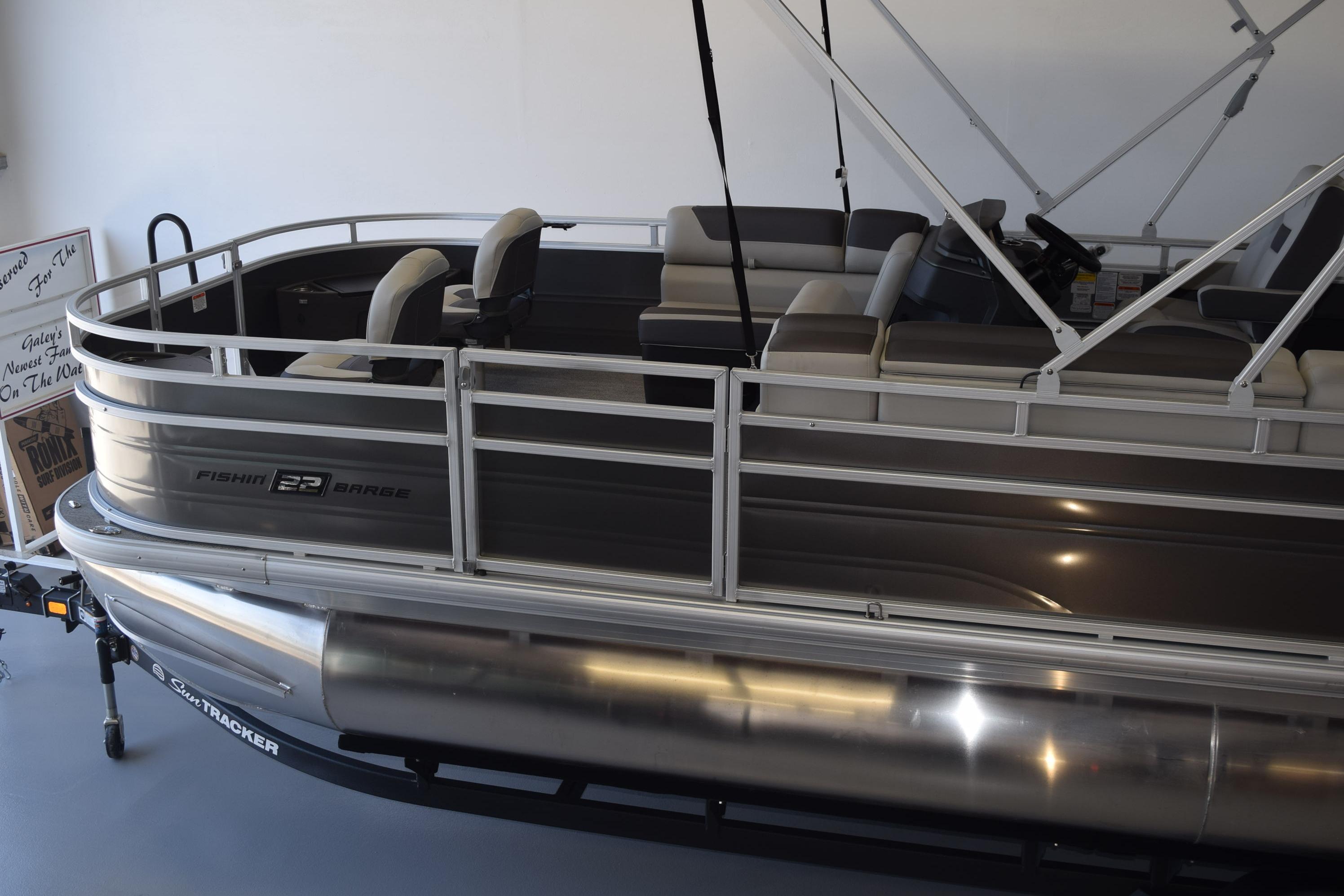 2026 Sun Tracker Fishin' Barge 22 DLX pontoon boat in showroom, side view.