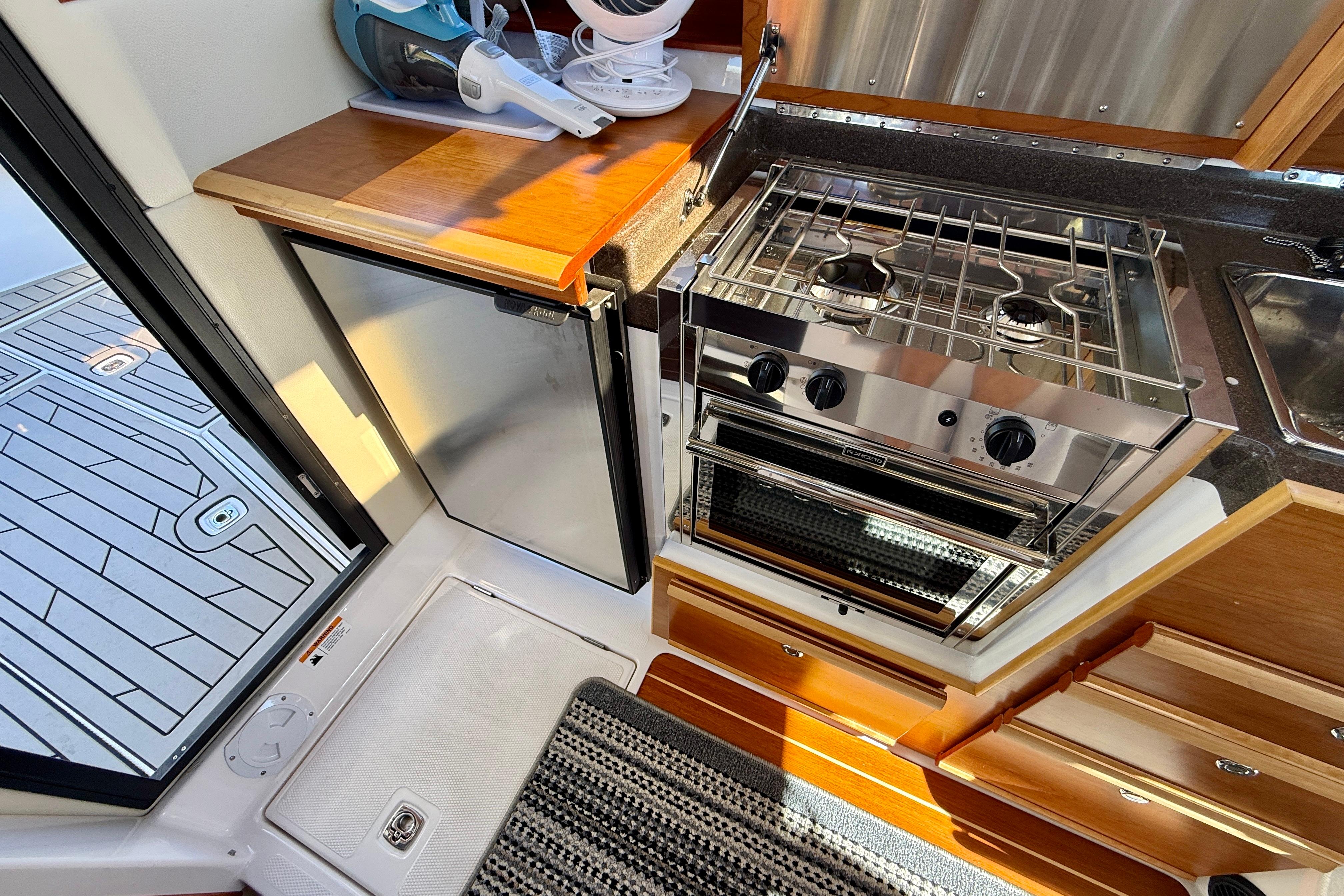 2023 Cutwater C-30 Sedan kitchen with stove, fridge, and wooden cabinetry.