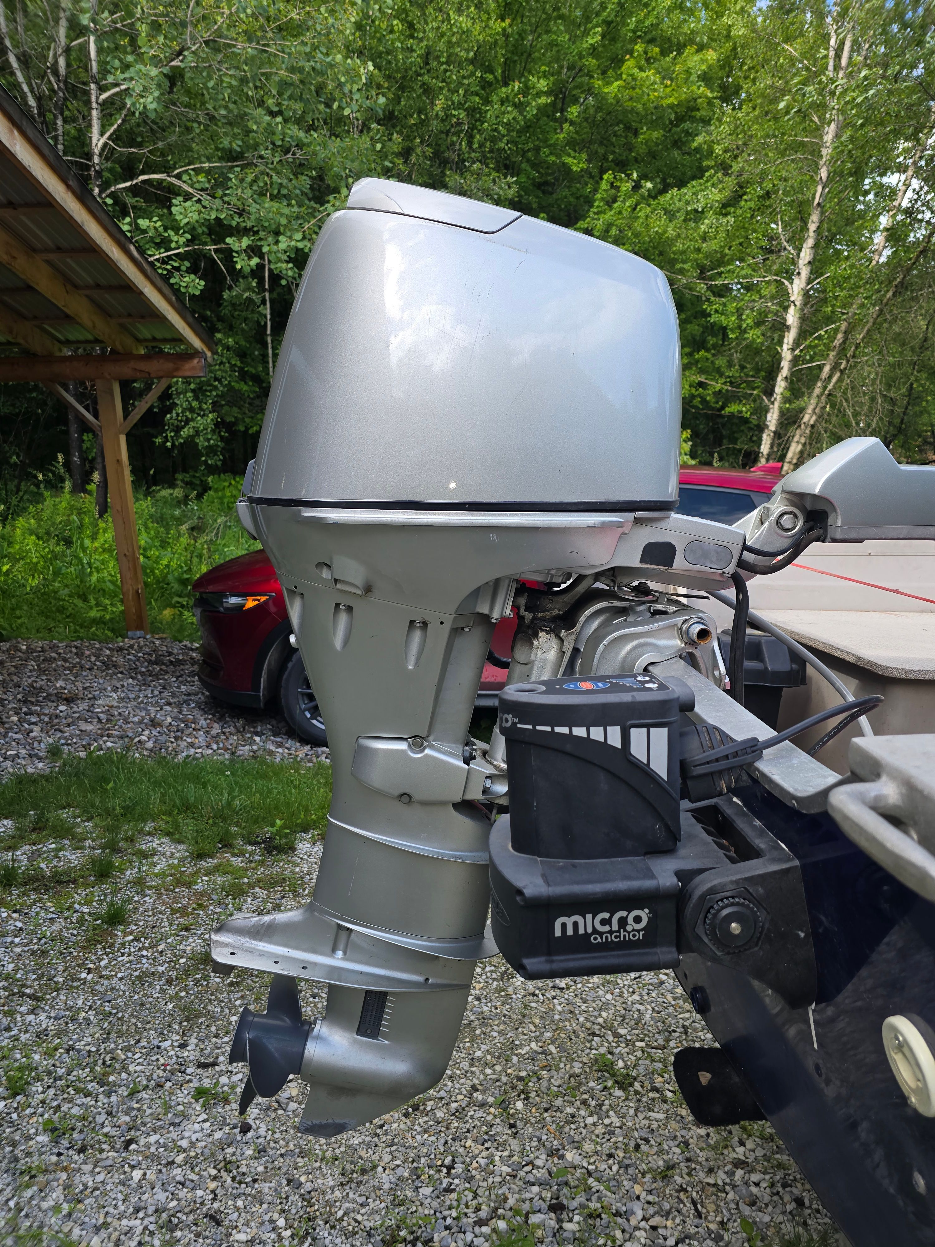 An outboard motor of a boat on a trailer, surrounded by trees and a car.