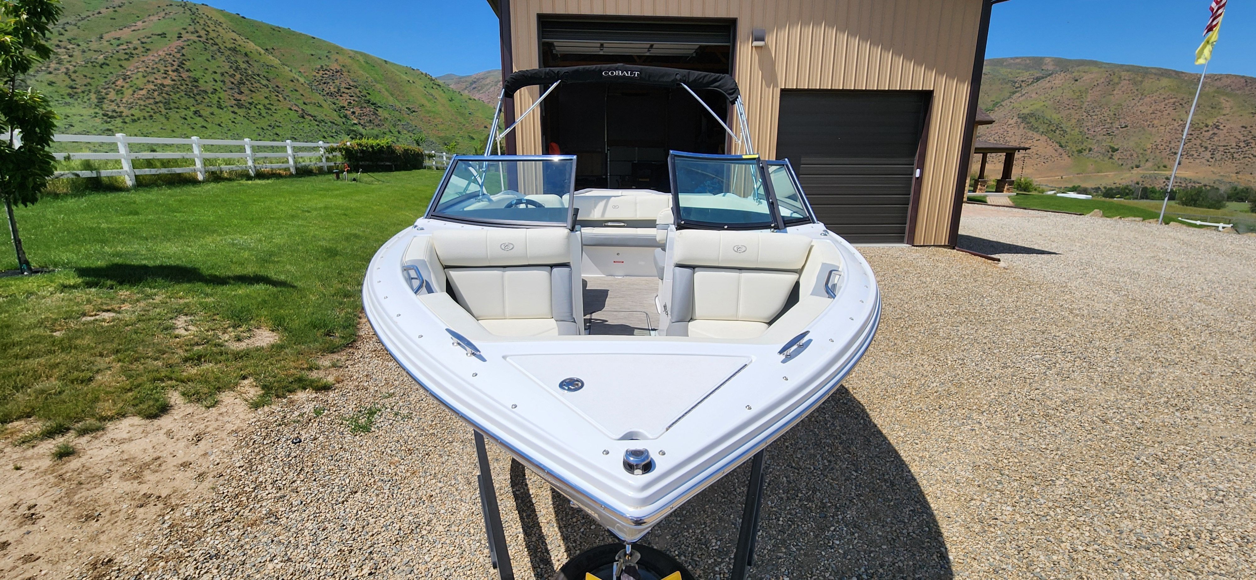 A Cobalt CS22 boat on a trailer in front of a garage in a rural setting.