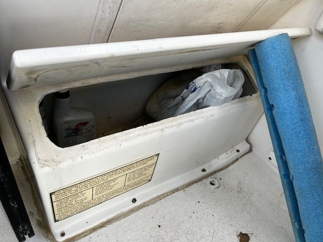 An open storage compartment on a boat with a bottle and a plastic bag inside.