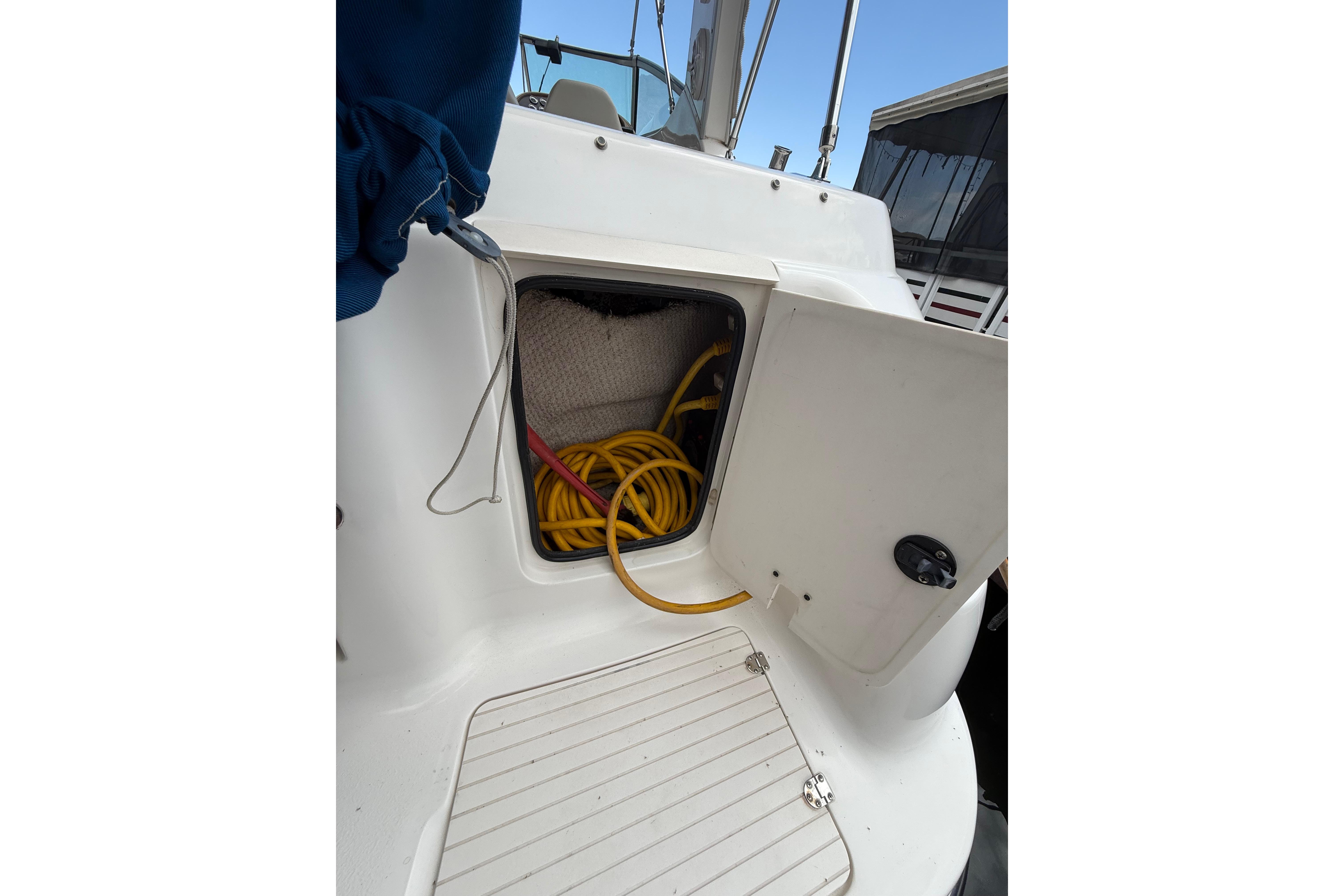 Open storage compartment on 1999 Chaparral Signature 300 boat with coiled yellow hose.