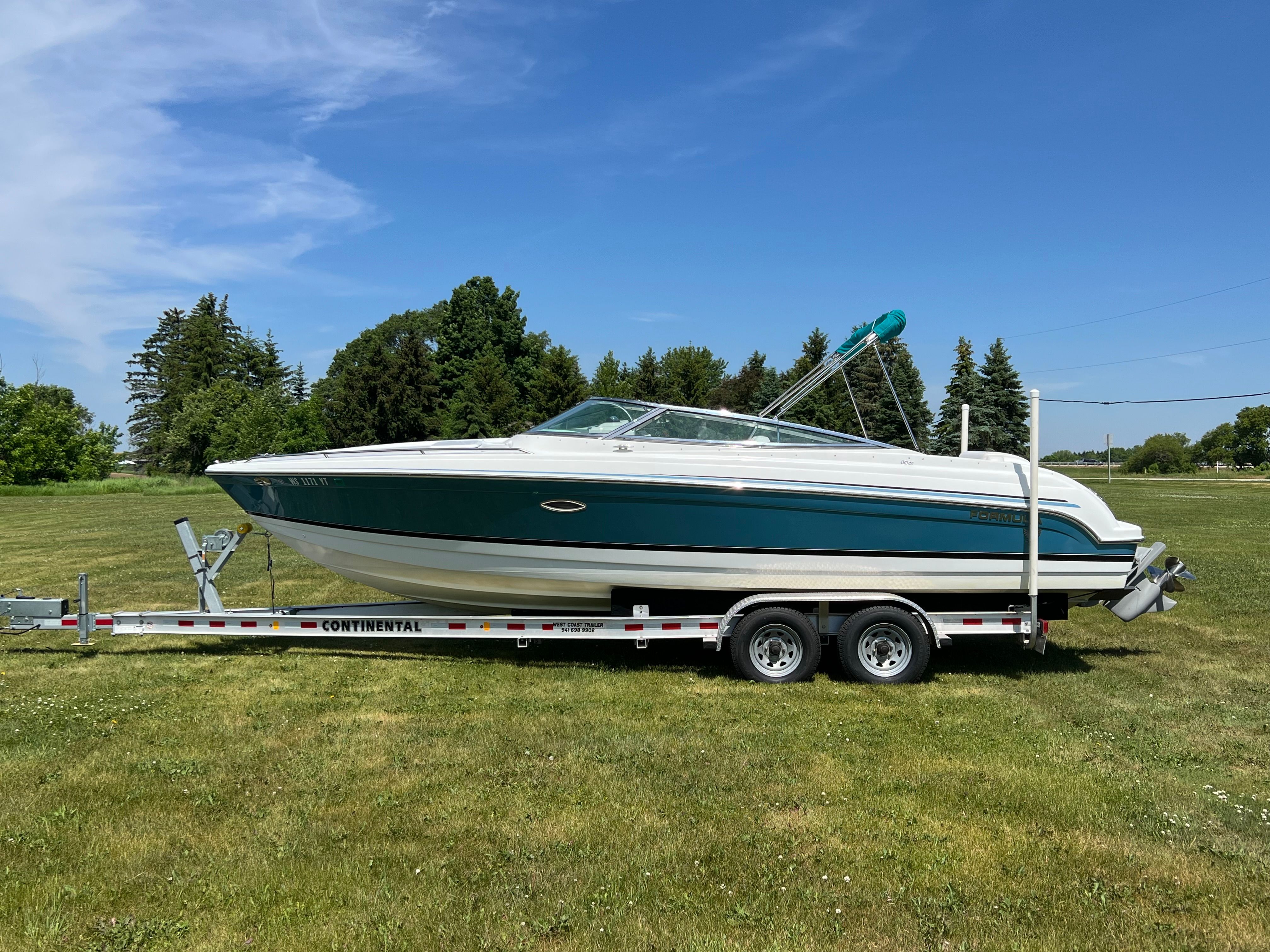 A 2005 Formula 260 Sun Sport on a trailer, surrounded by green grass and trees.