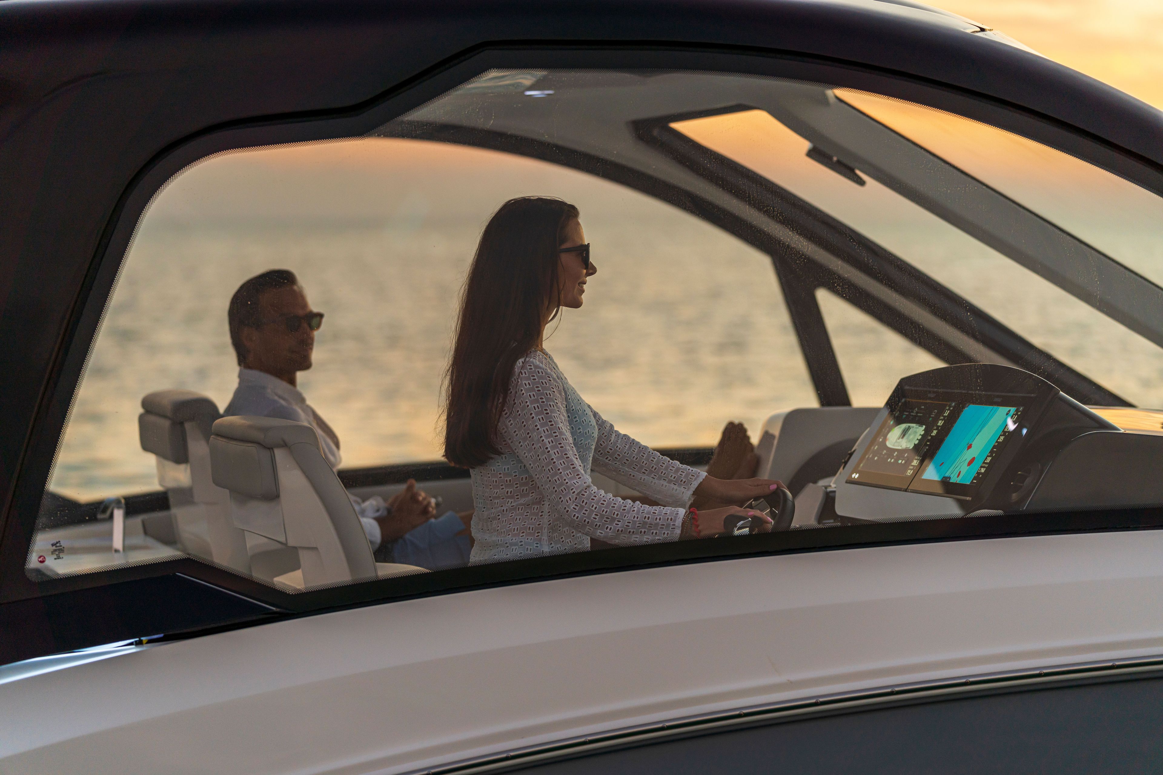 Two people sit in a modern boat with sleek interior as the sun sets.