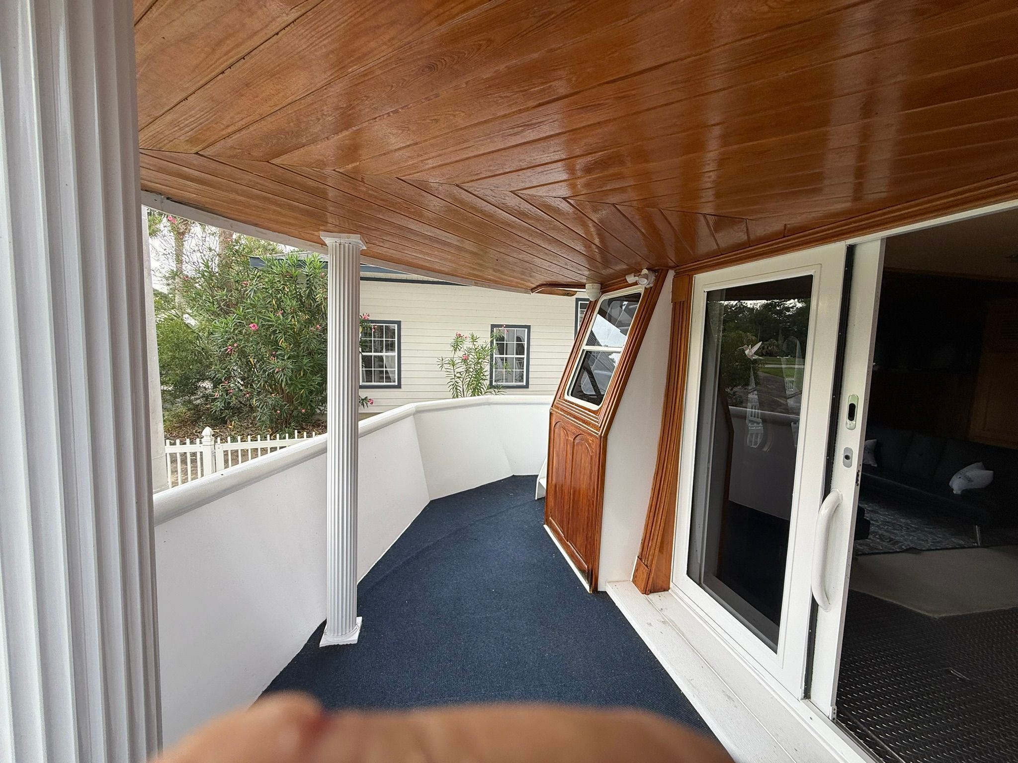 A covered area with wooden ceiling and blue carpet, next to a white railing.