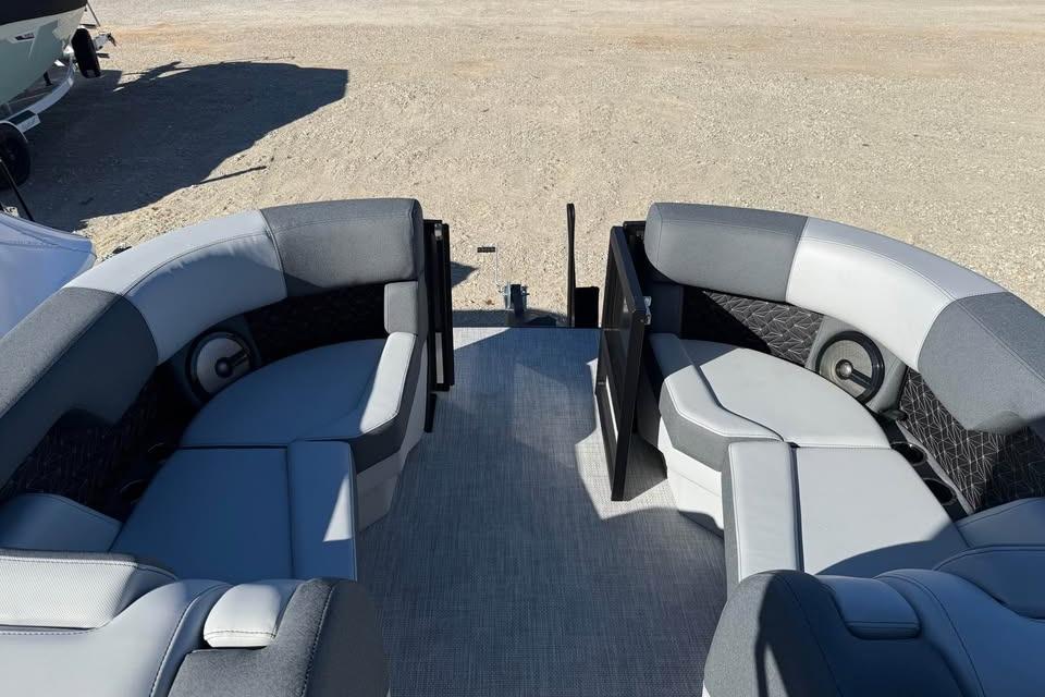 2026 Alera M 23L boat interior with gray seating and speakers, parked on sandy ground.
