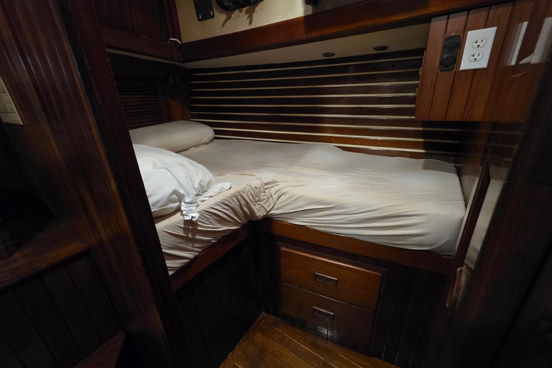Cozy cabin bed in 1982 Tayana 37 sailboat with wooden interior and storage drawers.