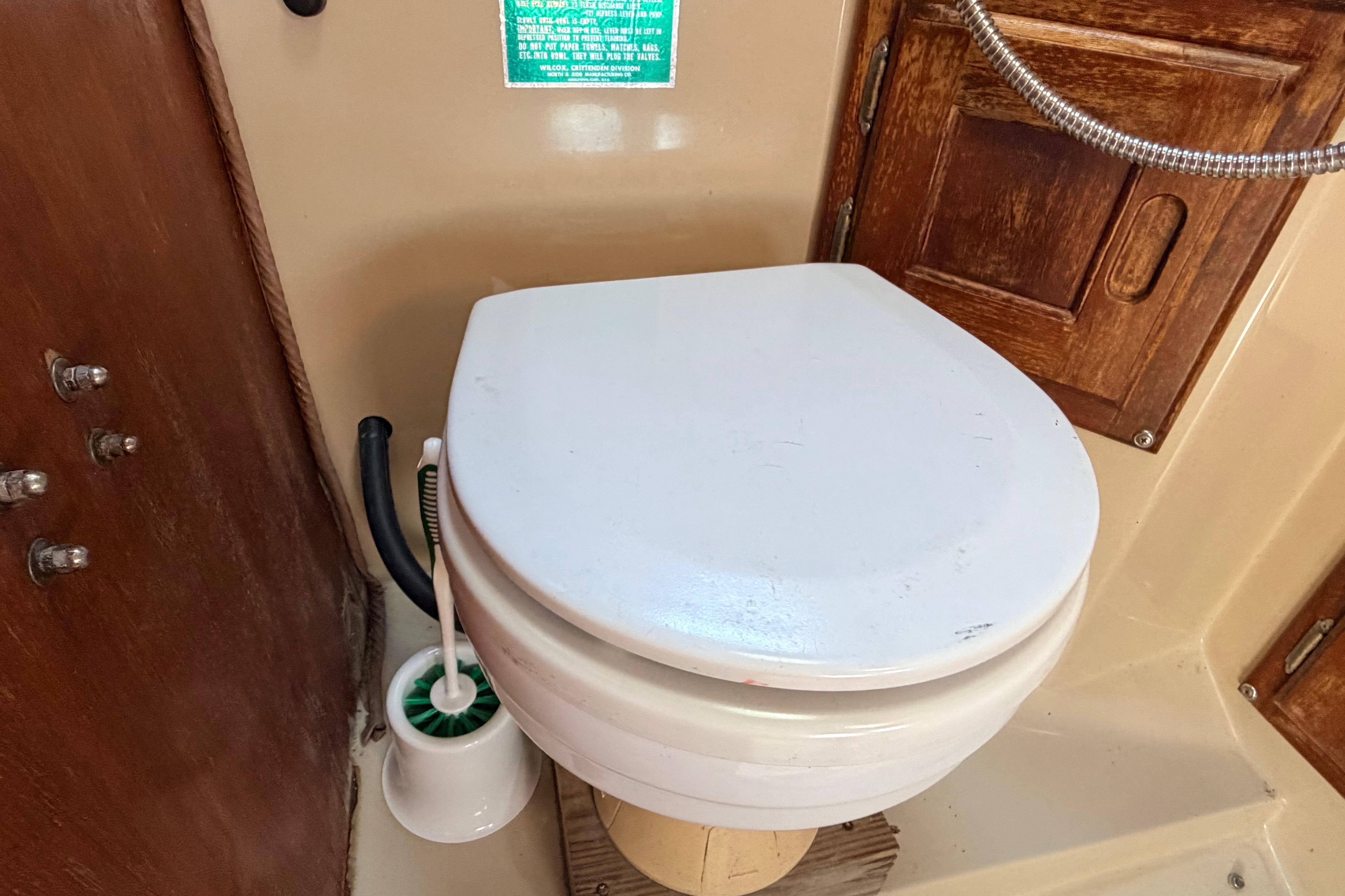 Boat bathroom with white toilet, wooden paneling, and cleaning brush on a 1981 Catalina 30.
