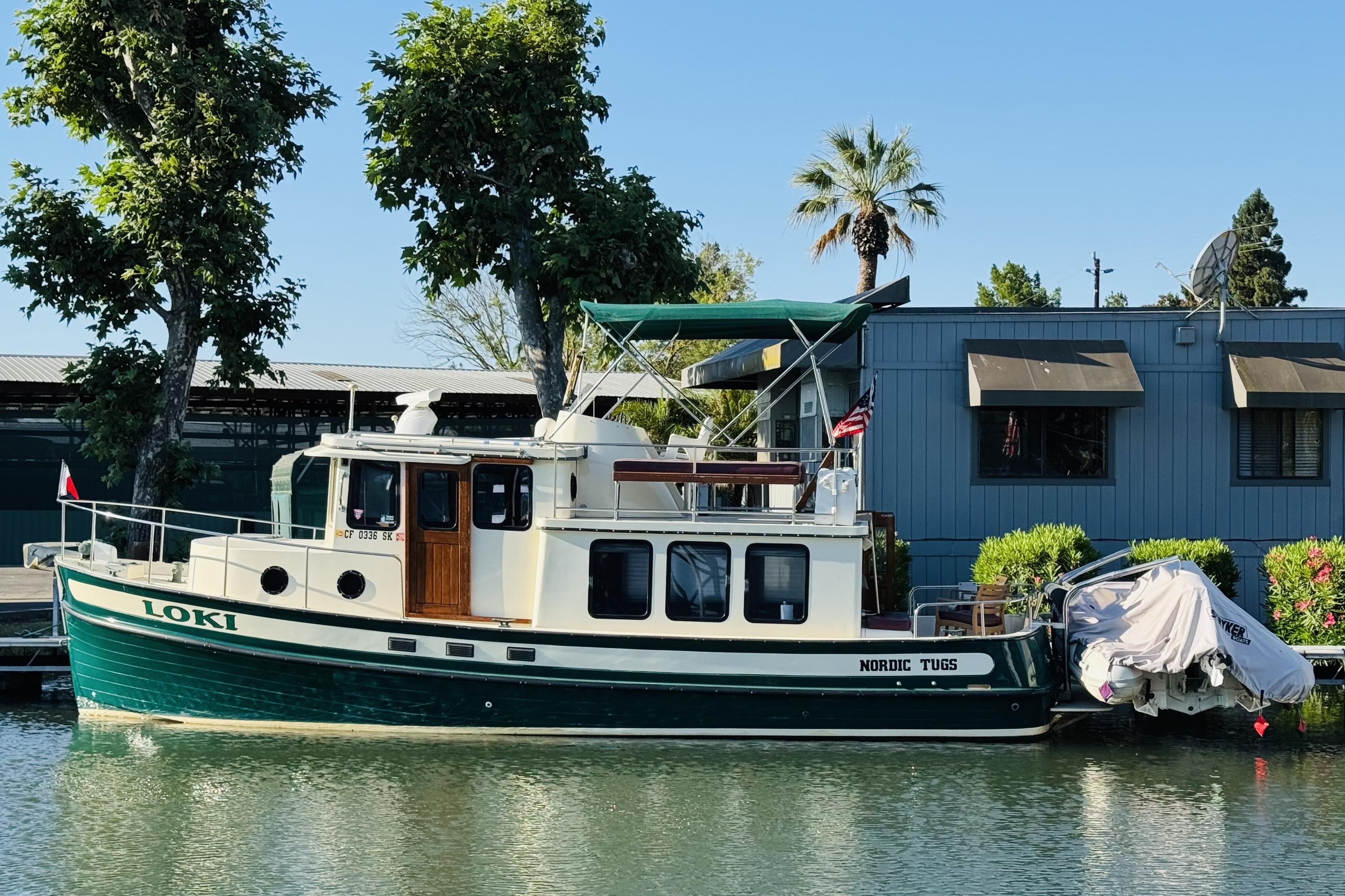 1996 Nordic Tug 32 boat docked by trees and building, named "Loki."
