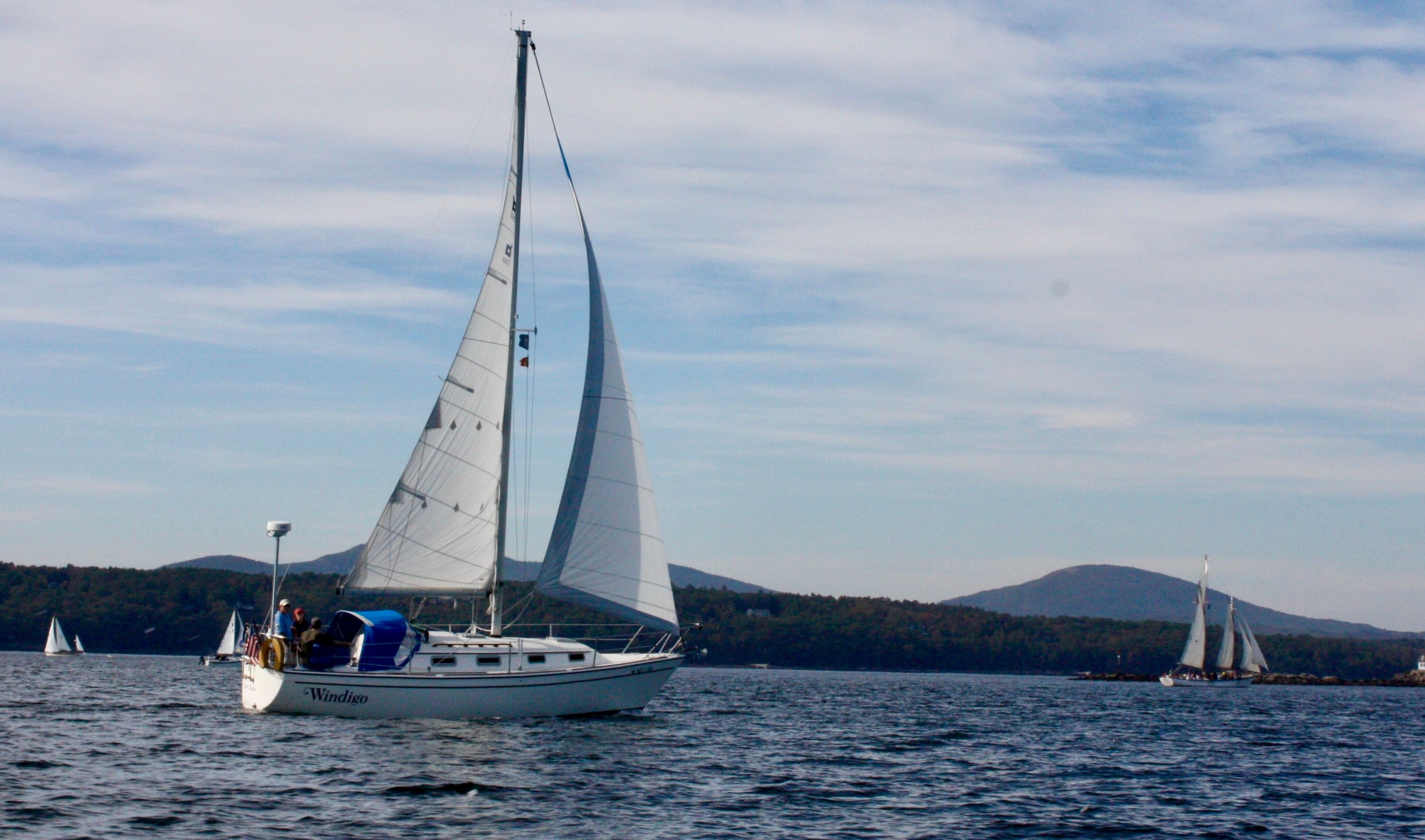 Sailboat on calm water with wooded hills in the background.