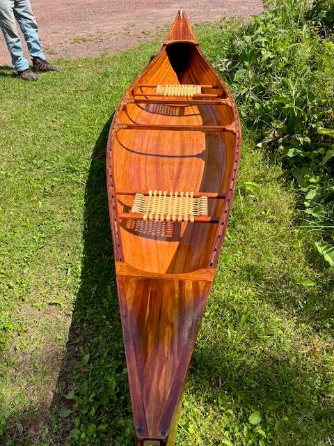 A handcrafted cedar strip canoe with woven seats on grass.