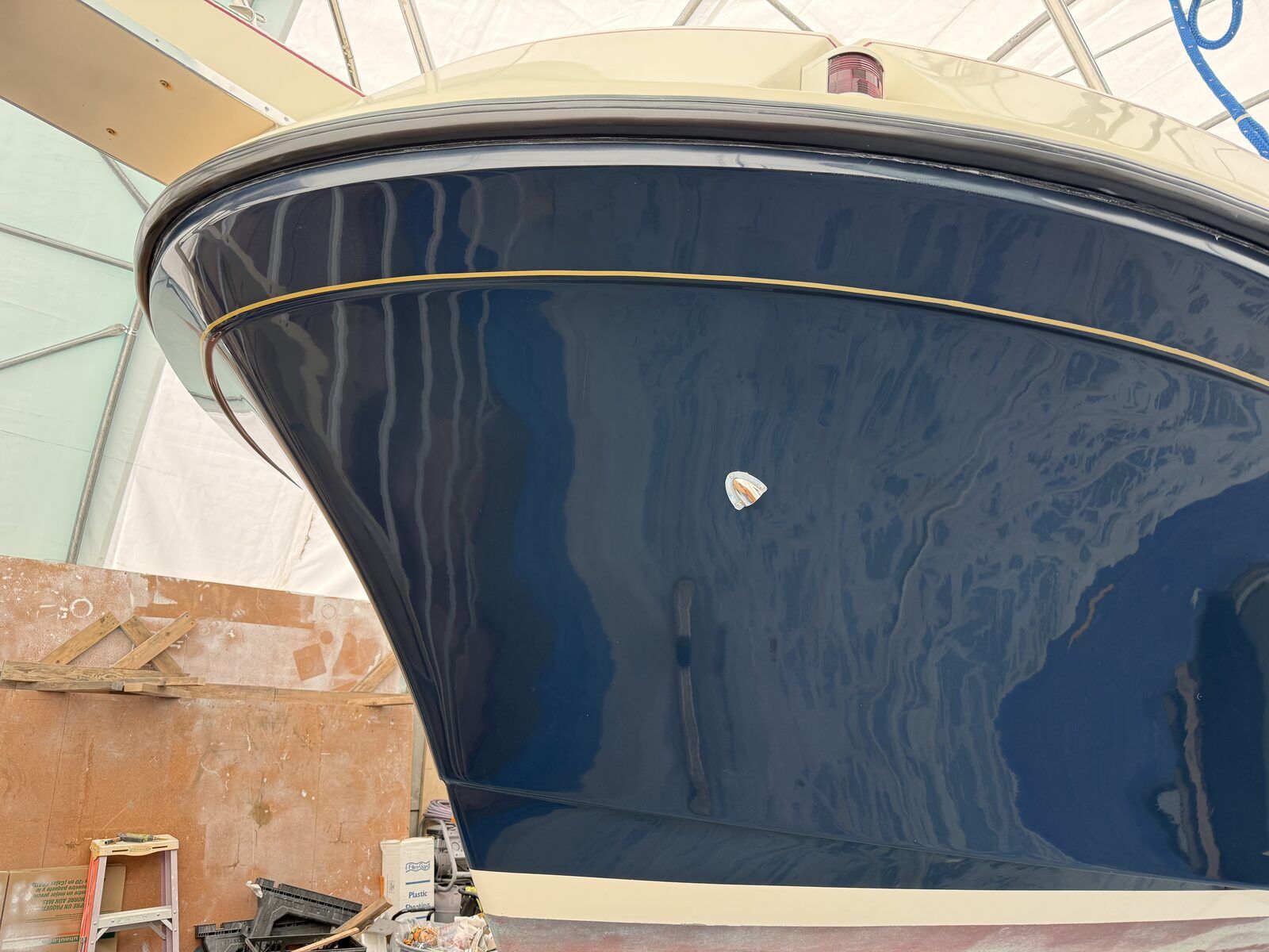 A blue boat with a cream stripe in a boatyard.