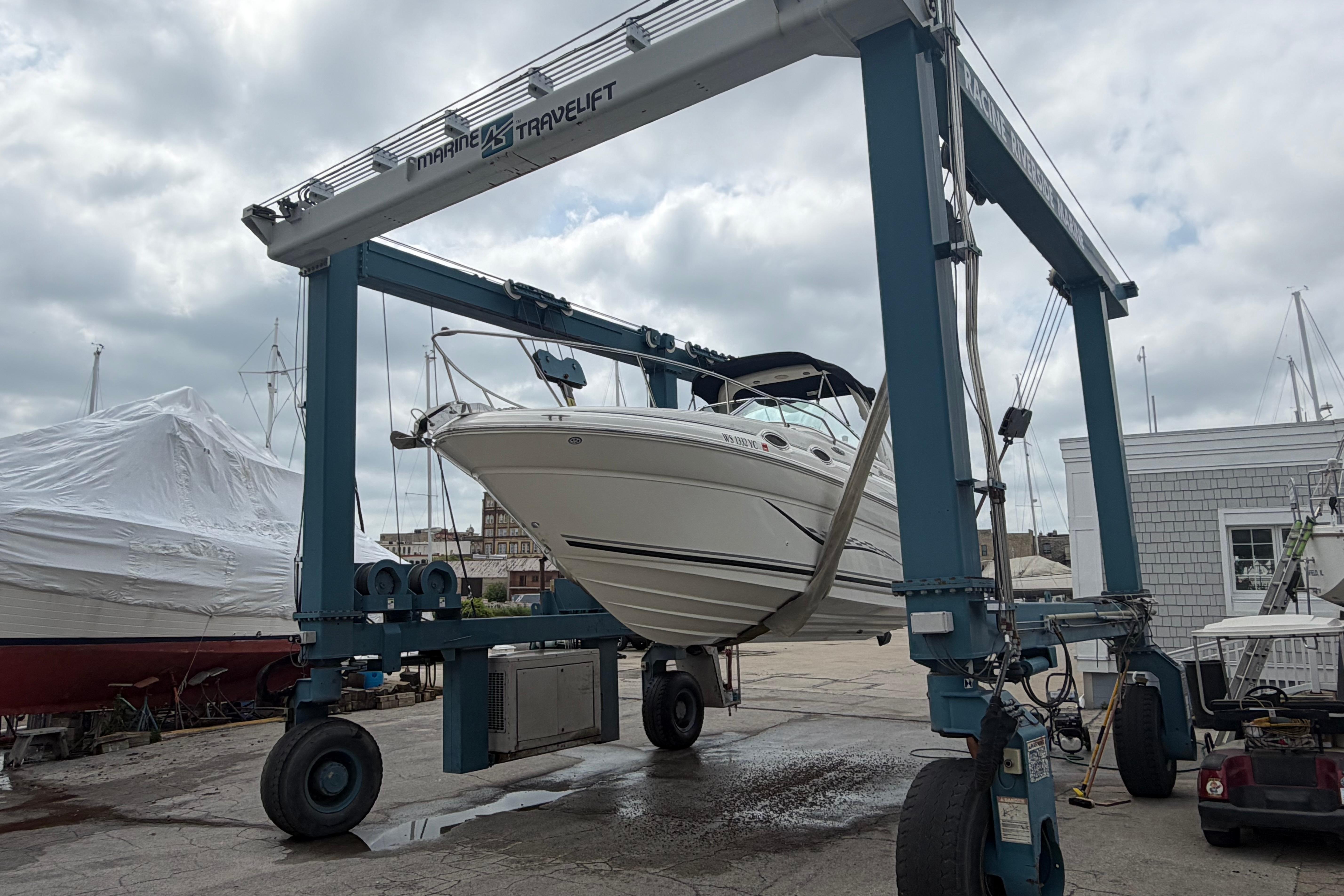 2004 Sea Ray Sundancer 260 boat lifted by a marine travel lift at a dockyard.