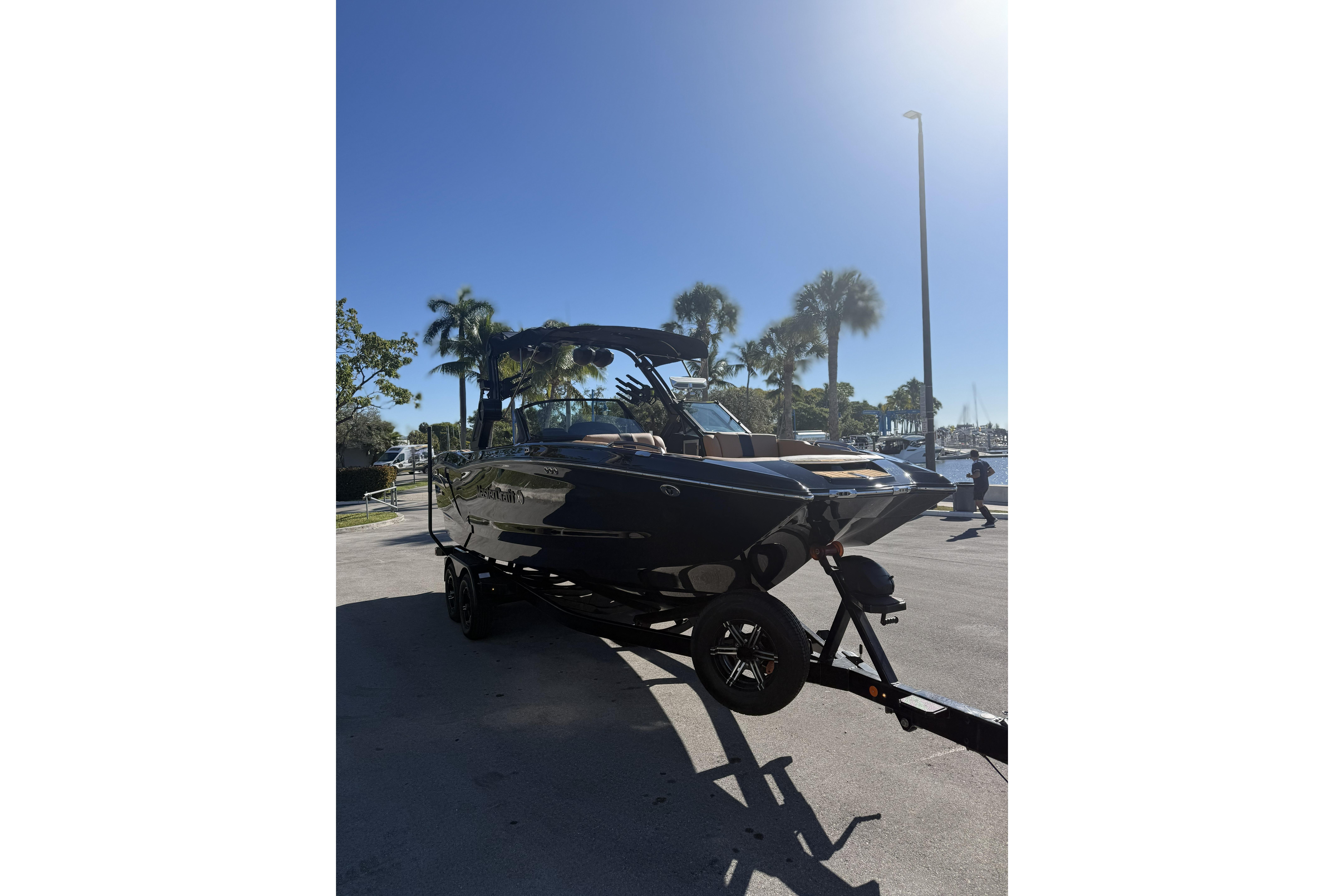 2024 MasterCraft X24 boat on trailer under clear blue sky with palm trees.