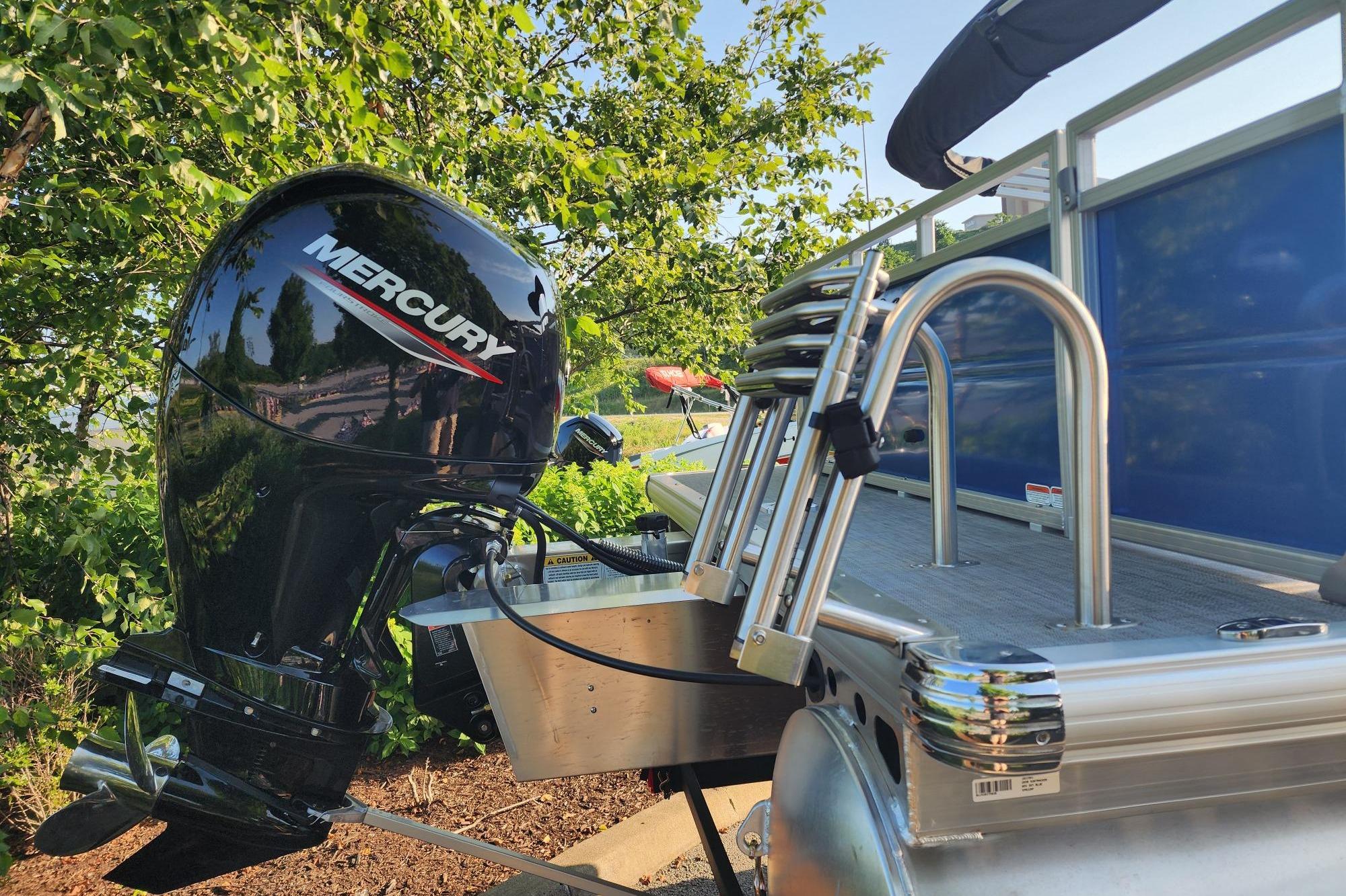 2026 Sun Tracker Party Barge 22 RF DLX with Mercury outboard motor, docked near lush greenery.