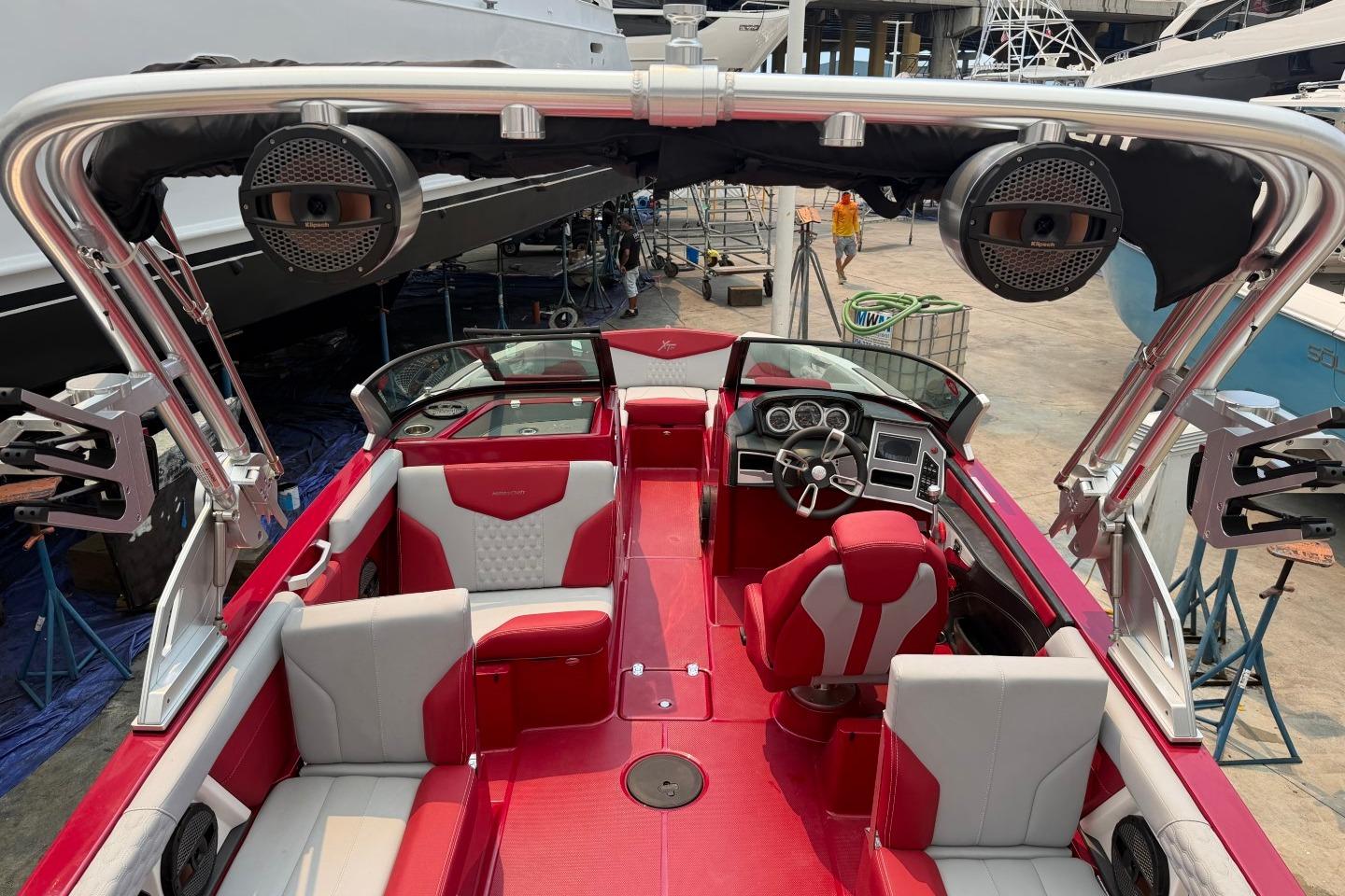2023 MasterCraft X24 boat interior with red and white seating, advanced dashboard, and speakers.
