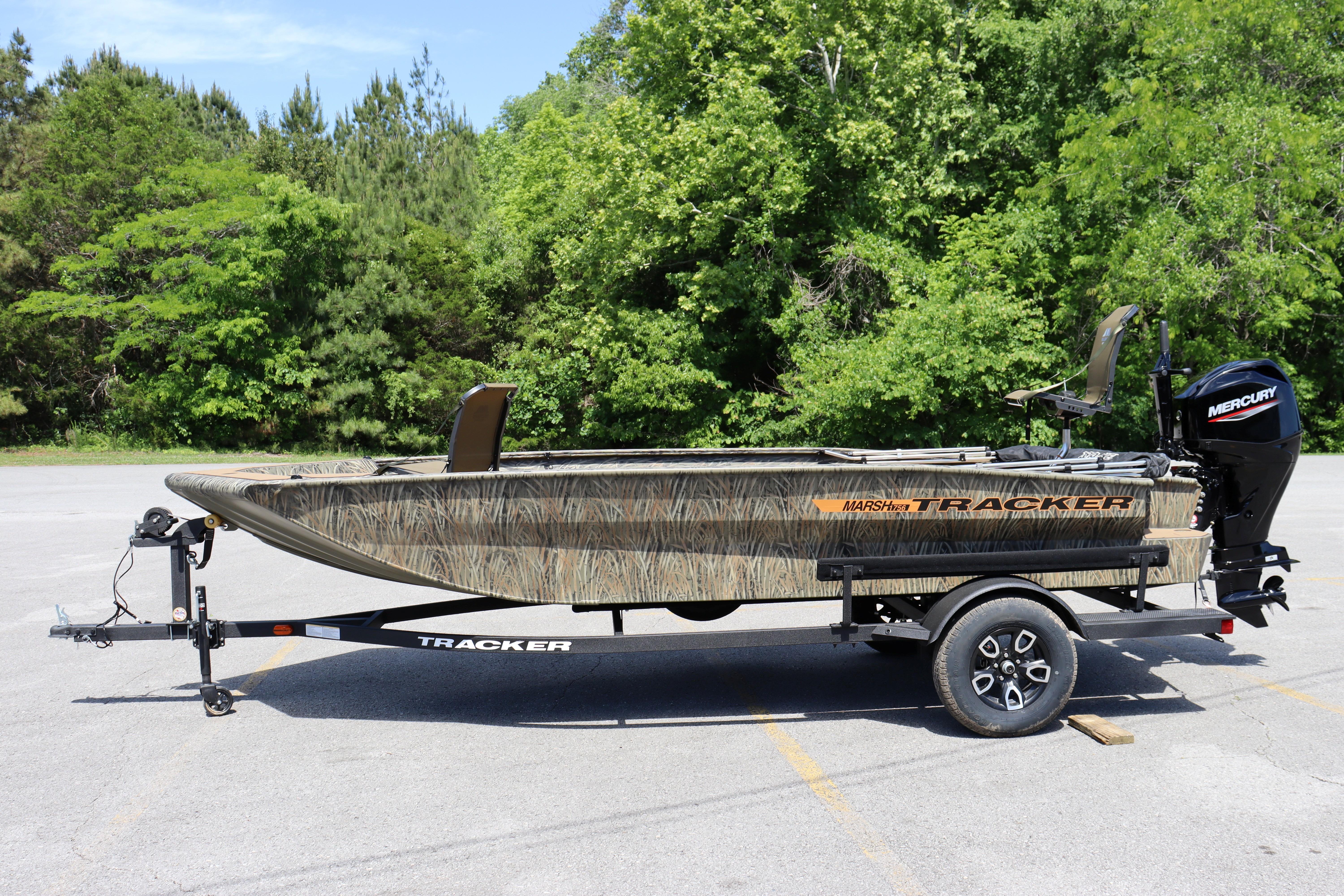 2026 Tracker Grizzly 1756 T Marsh boat on trailer, parked outdoors with green trees.