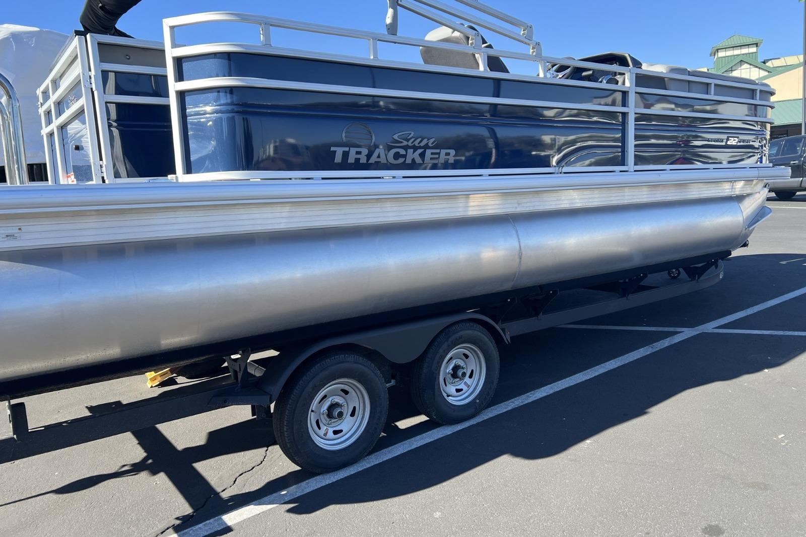 2026 Sun Tracker SportFish 22 DLX pontoon boat on trailer in parking lot.
