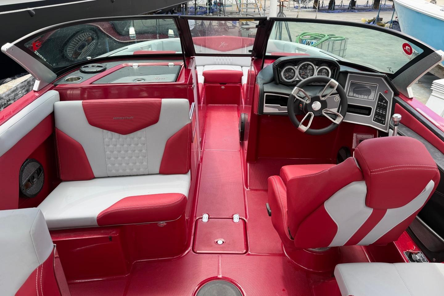 2023 MasterCraft X24 boat interior with red and white seating, modern dashboard, and steering wheel.