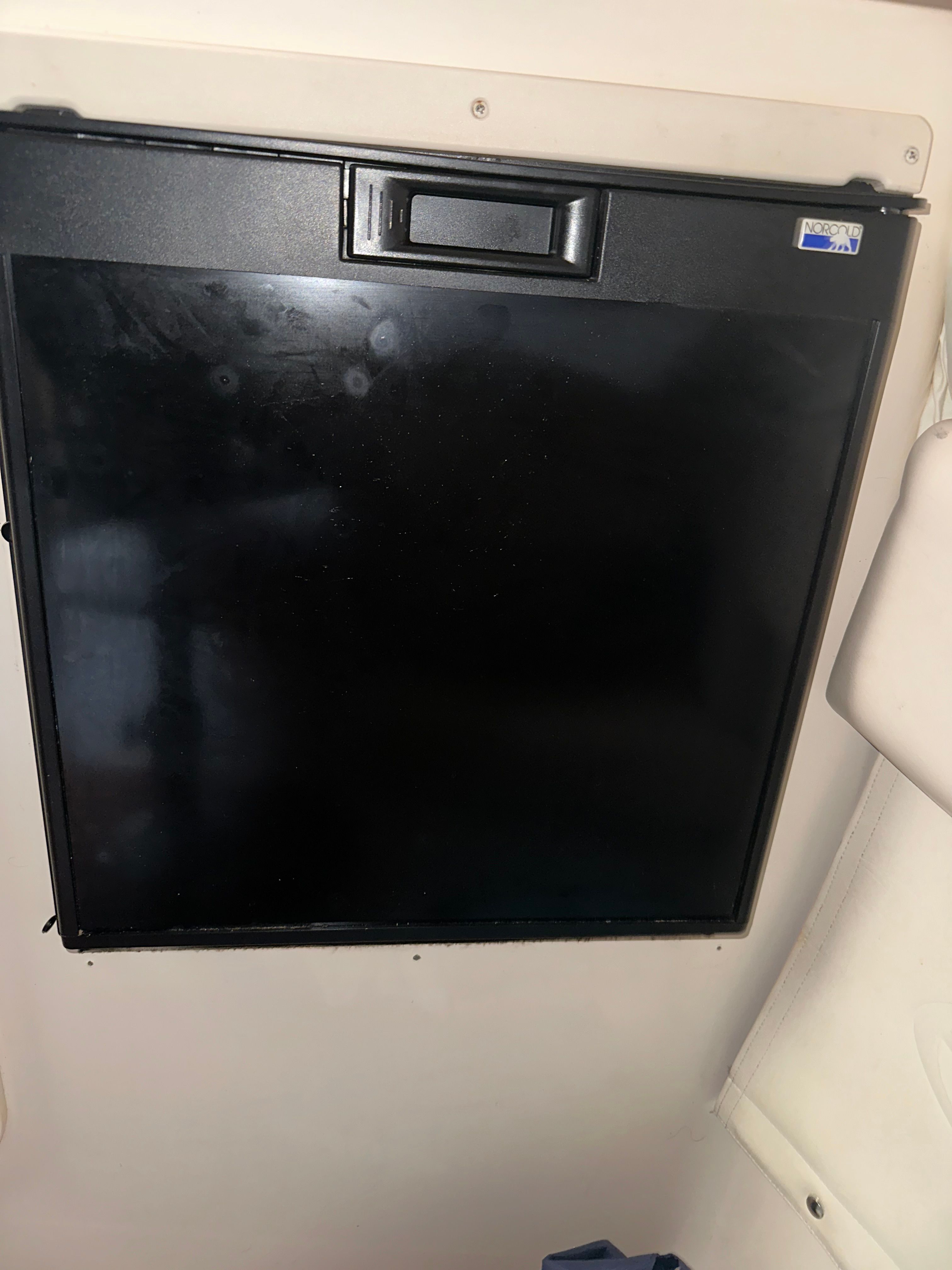 A refrigerator in a boat cabin, built into a white wall.