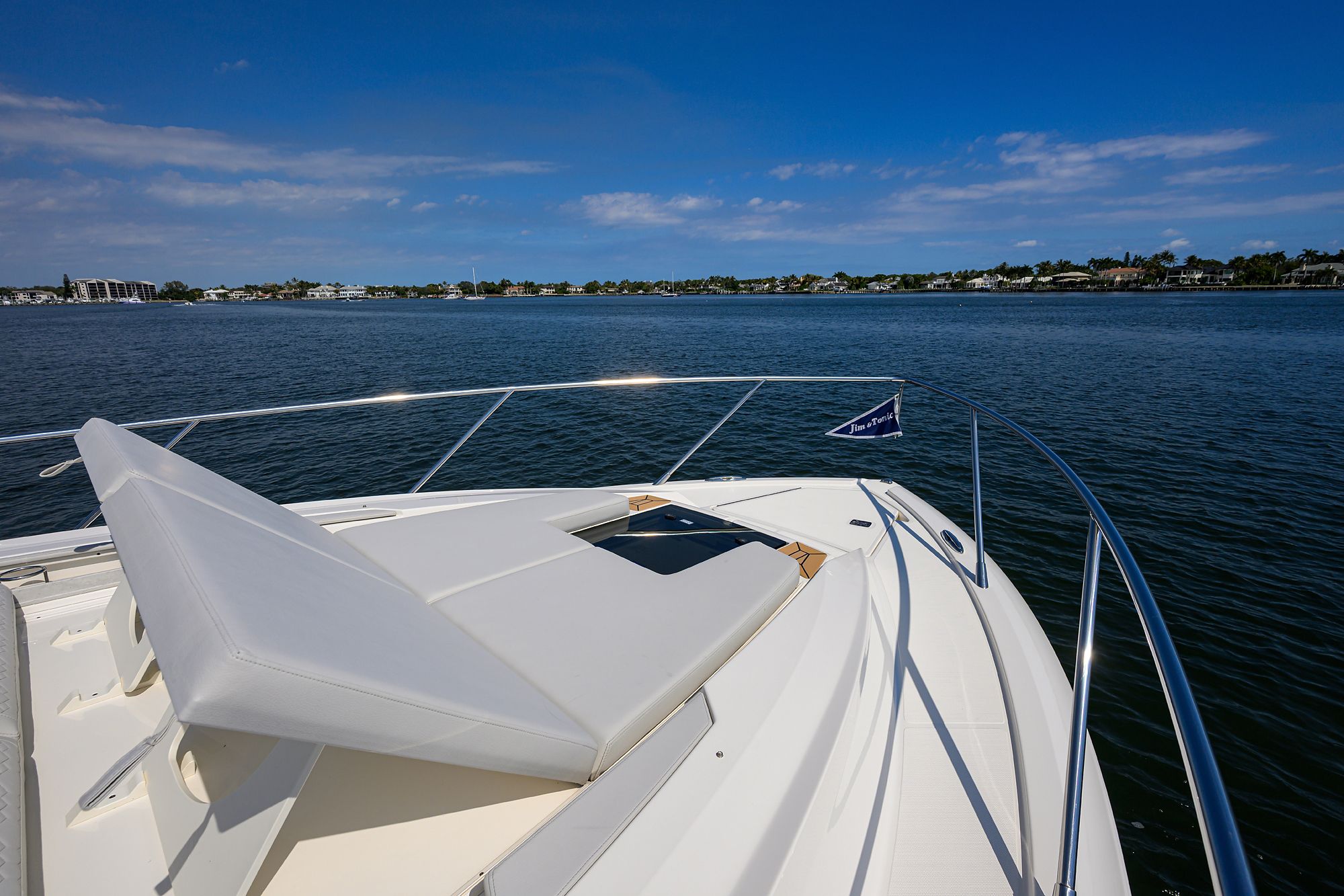 A luxury boat with a sunbed cruises on calm water under a blue sky.