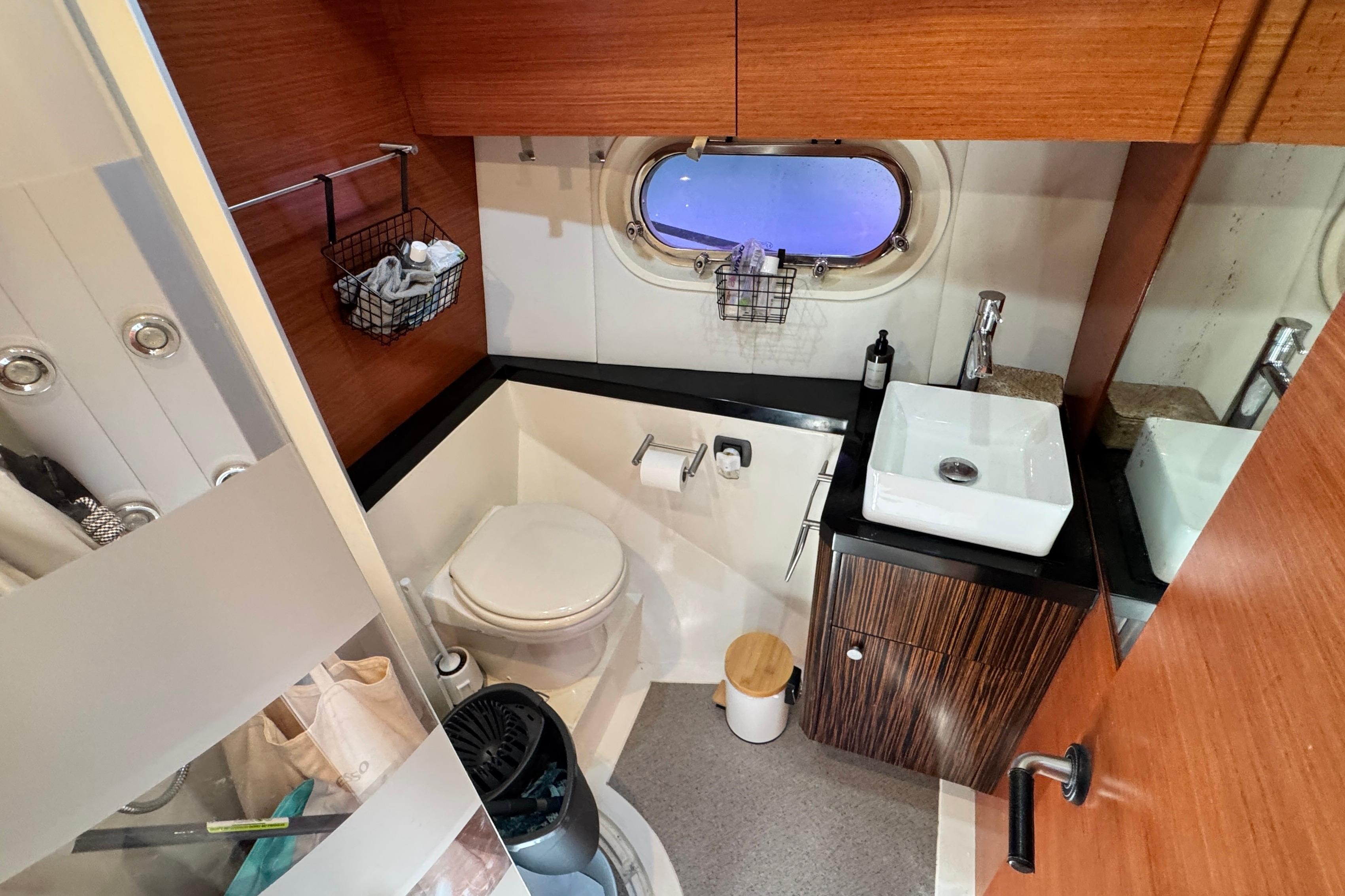 Compact boat bathroom with wooden accents, featuring a sink, toilet, and porthole window. Doma 5, 2007.