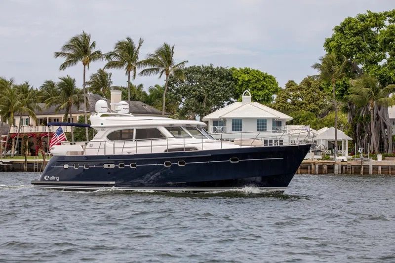 Luxury yacht on water near tropical shoreline with palm trees and houses.