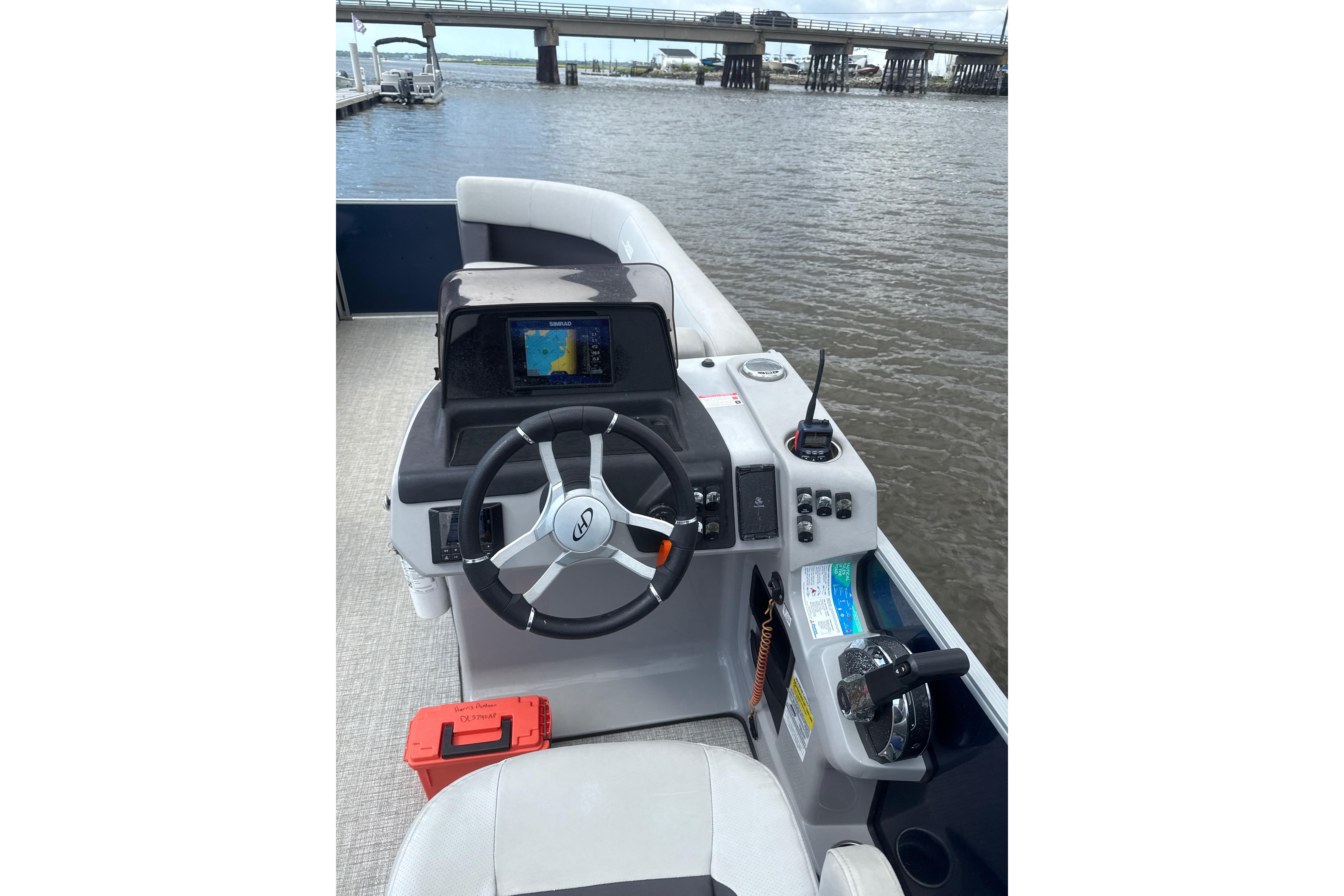 2024 Harris HCX23 boat helm with steering wheel and navigation system on a calm river.