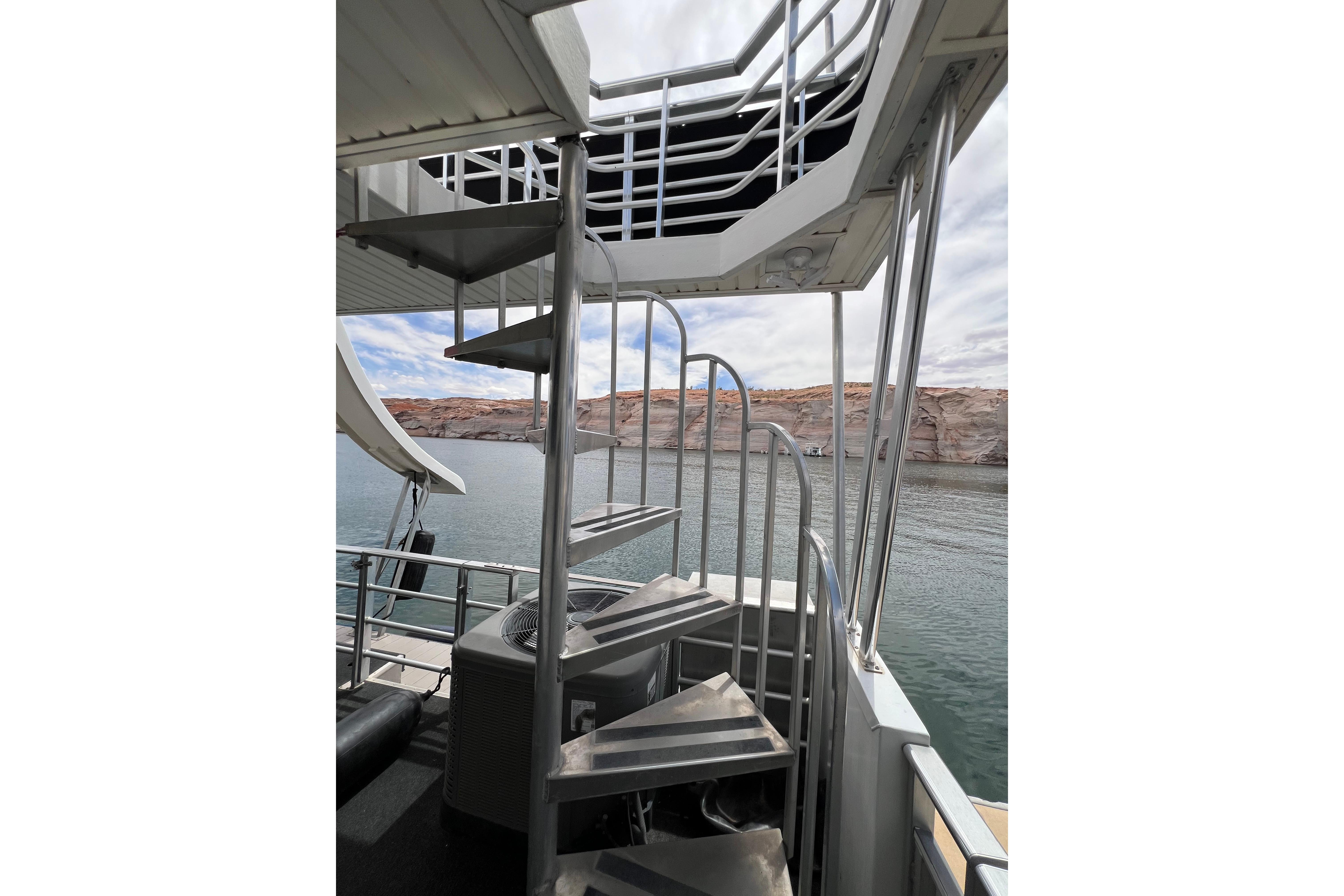 Spiral staircase on 2013 Destination Yacht Lotta Yachta, overlooking serene waters and rocky shoreline.