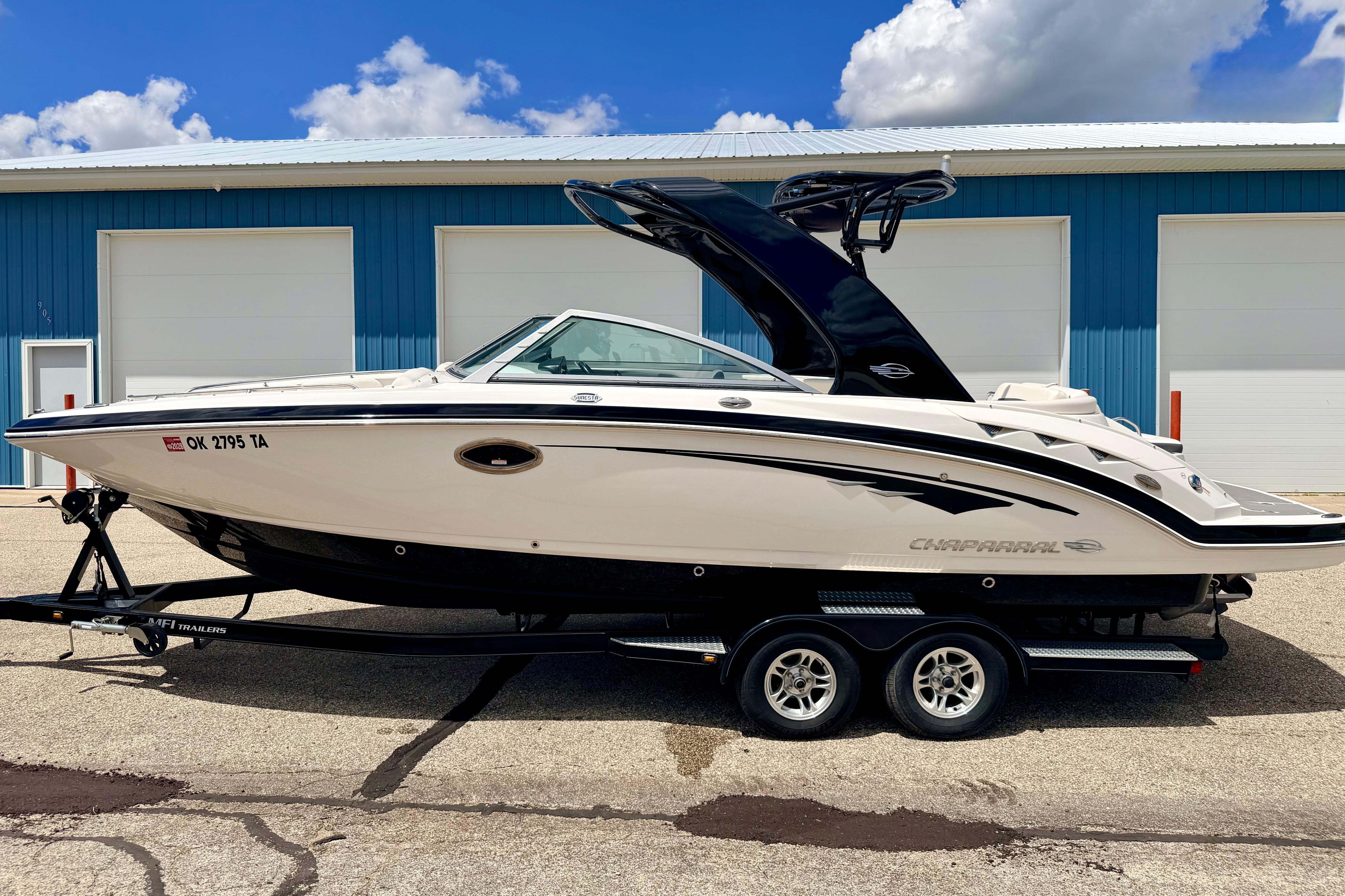 2015 Chaparral Sunesta 264 boat on trailer, parked near blue building.