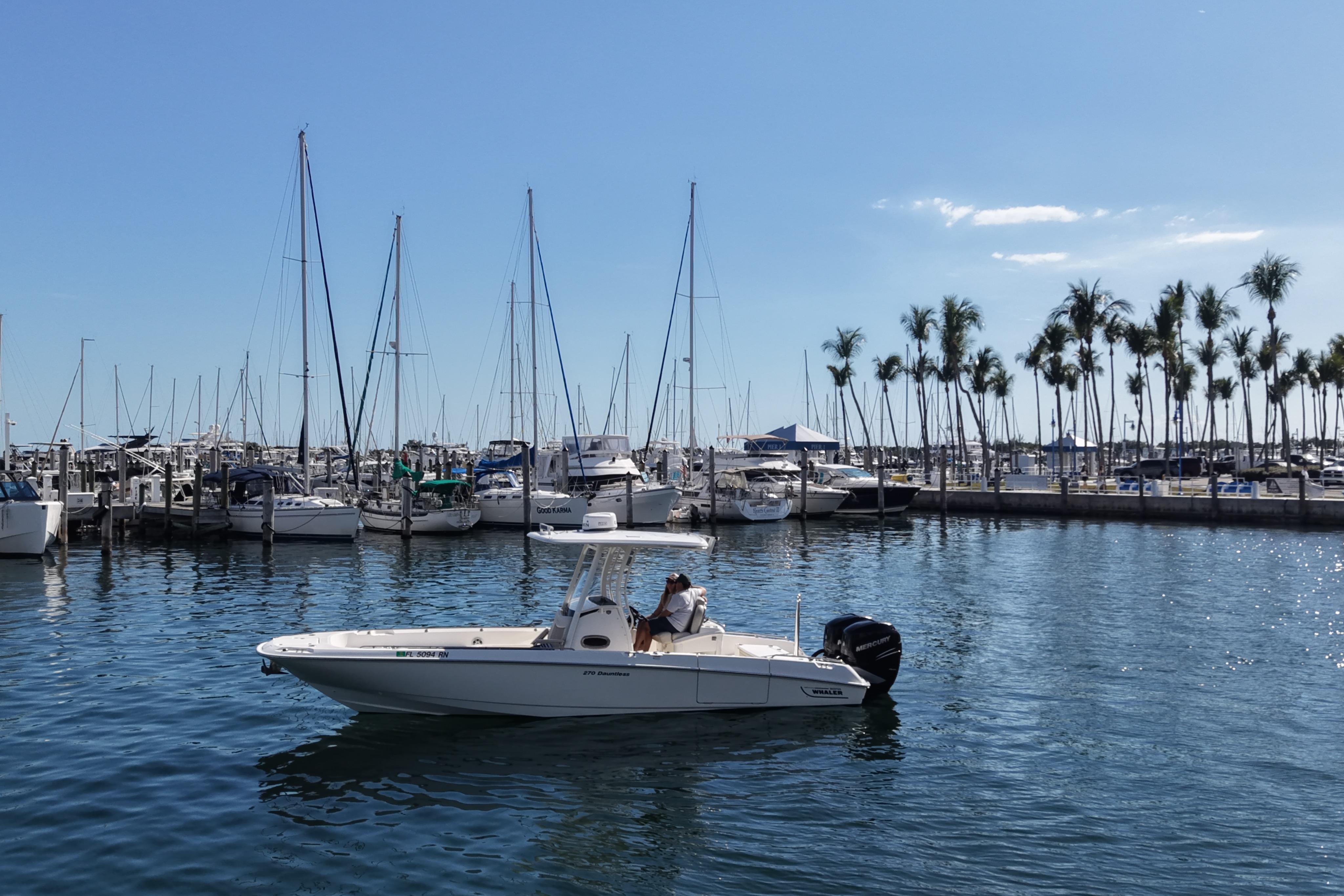 2018 Boston Whaler 270 Dauntless boat in marina with sailboats and palm trees.