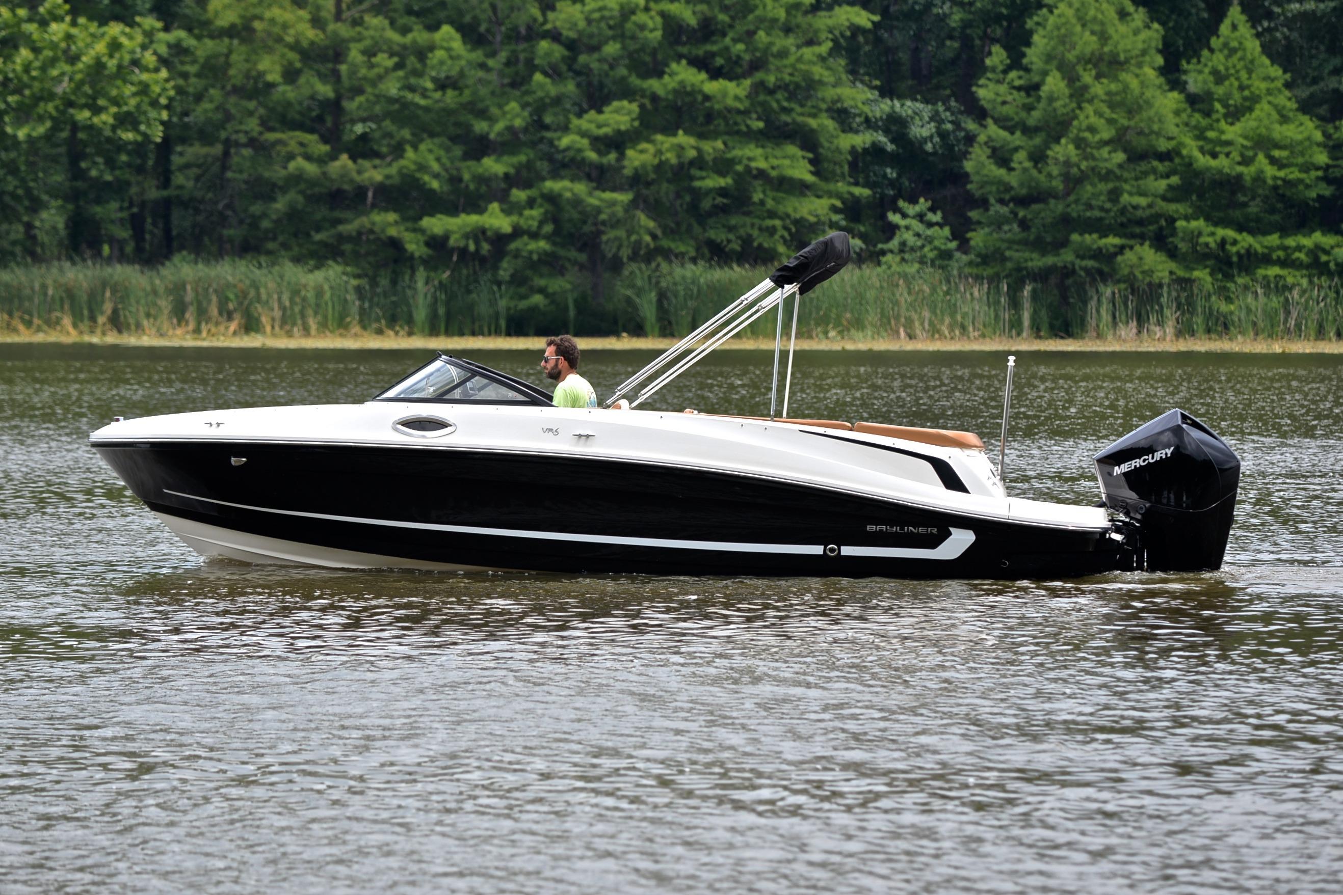 2019 Bayliner VR6 Bowrider OB on a calm lake with lush green background.