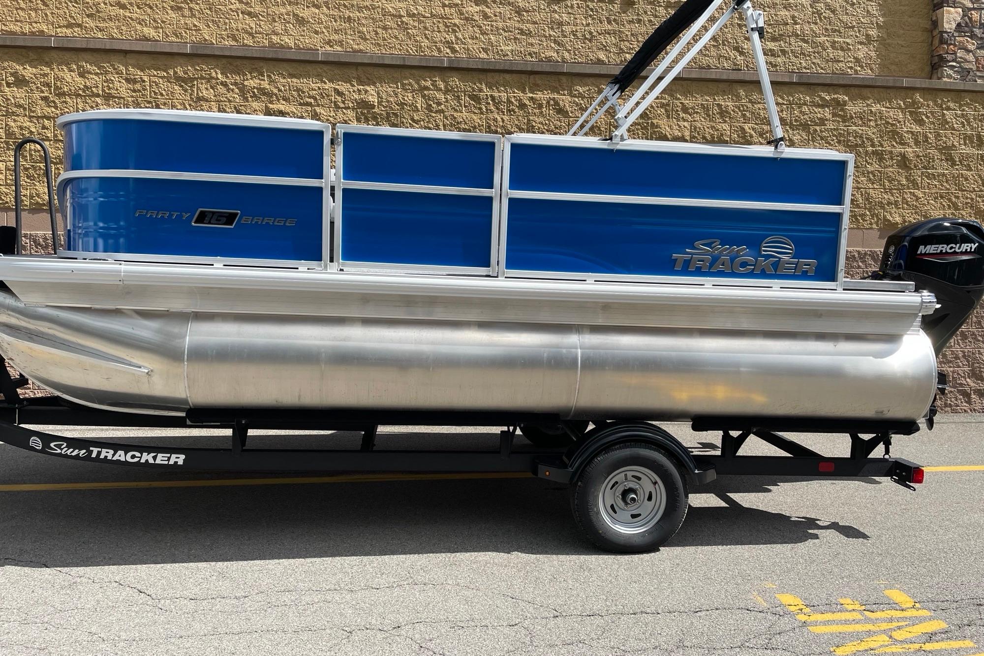 2026 Sun Tracker Party Barge 16 DLX pontoon boat on trailer, blue and silver design.