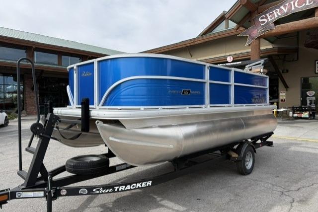 2026 Sun Tracker Party Barge 16 DLX pontoon boat on trailer, parked outside service center.