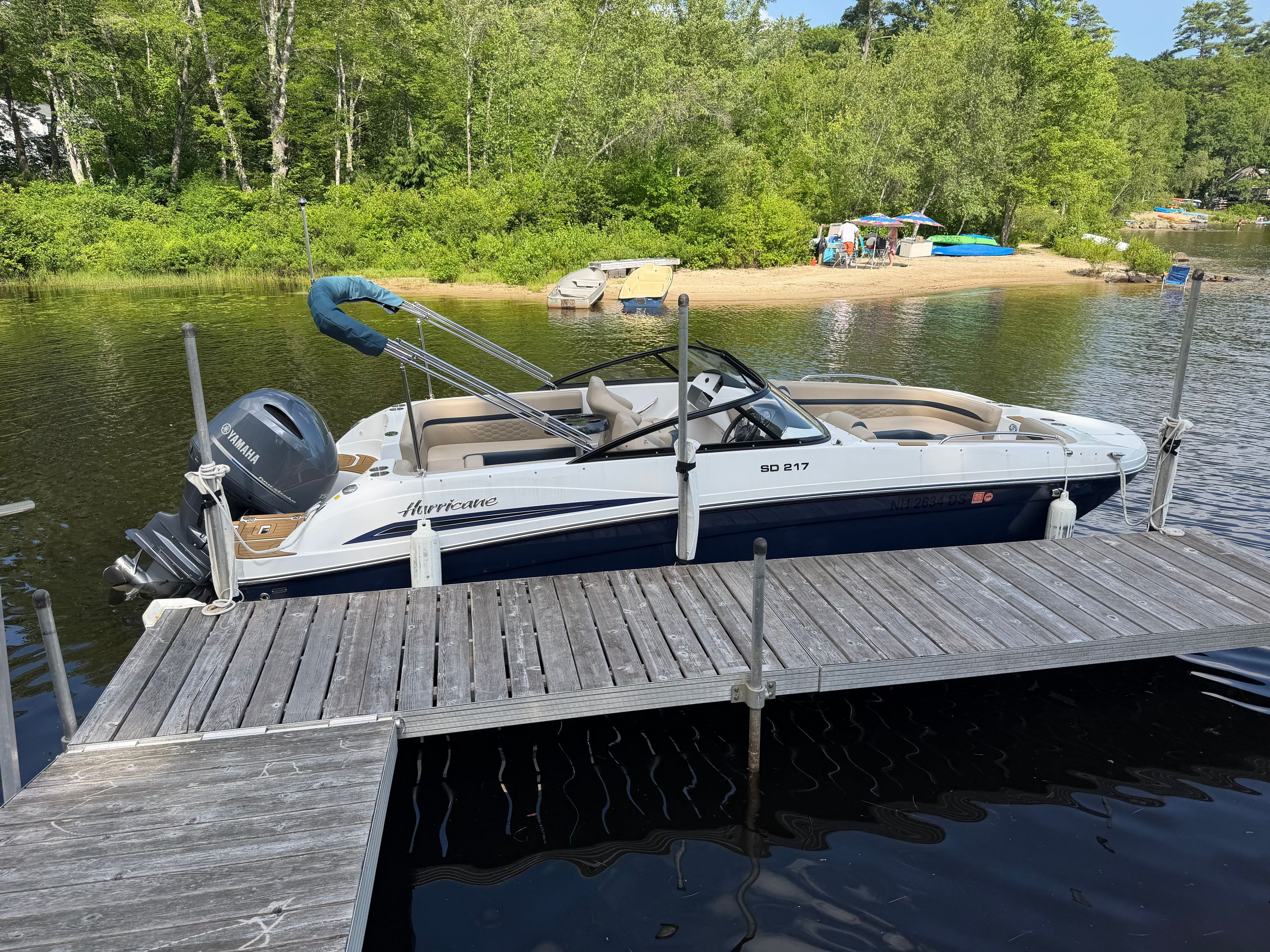 2022 Hurricane SunDeck 217 OB docked at a serene lake with a green shoreline.