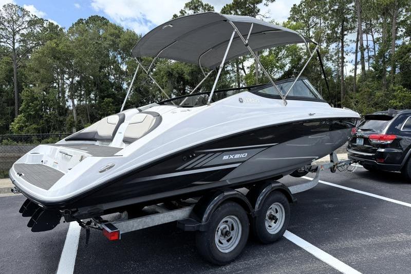 2017 Yamaha Boats SX210 on trailer, parked in a lot with trees in the background.