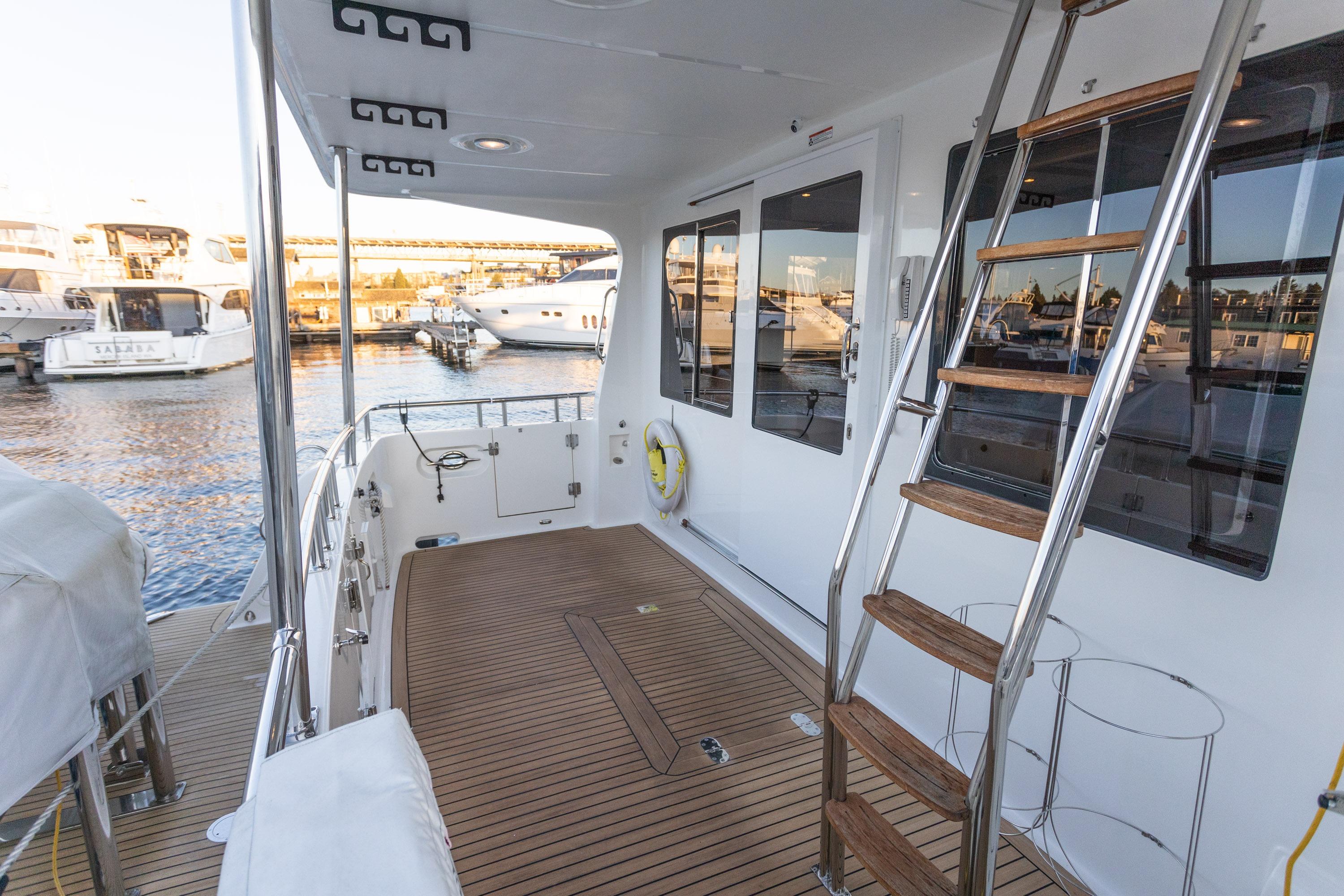 2021 North Pacific 49 Pilothouse yacht deck with wooden flooring and ladder, docked at marina.