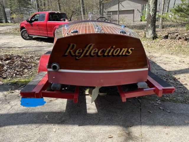 A 1938 Chris-Craft Custom Deluxe Runabout on a trailer. The name "Reflections" is visible on the stern.