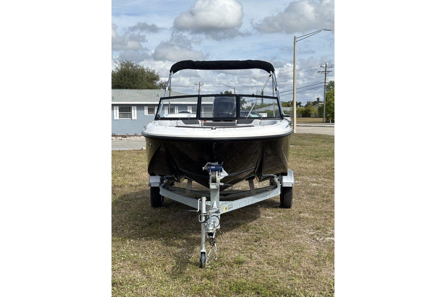 2025 Bayliner Element M17 boat on trailer, parked on grass under cloudy sky.