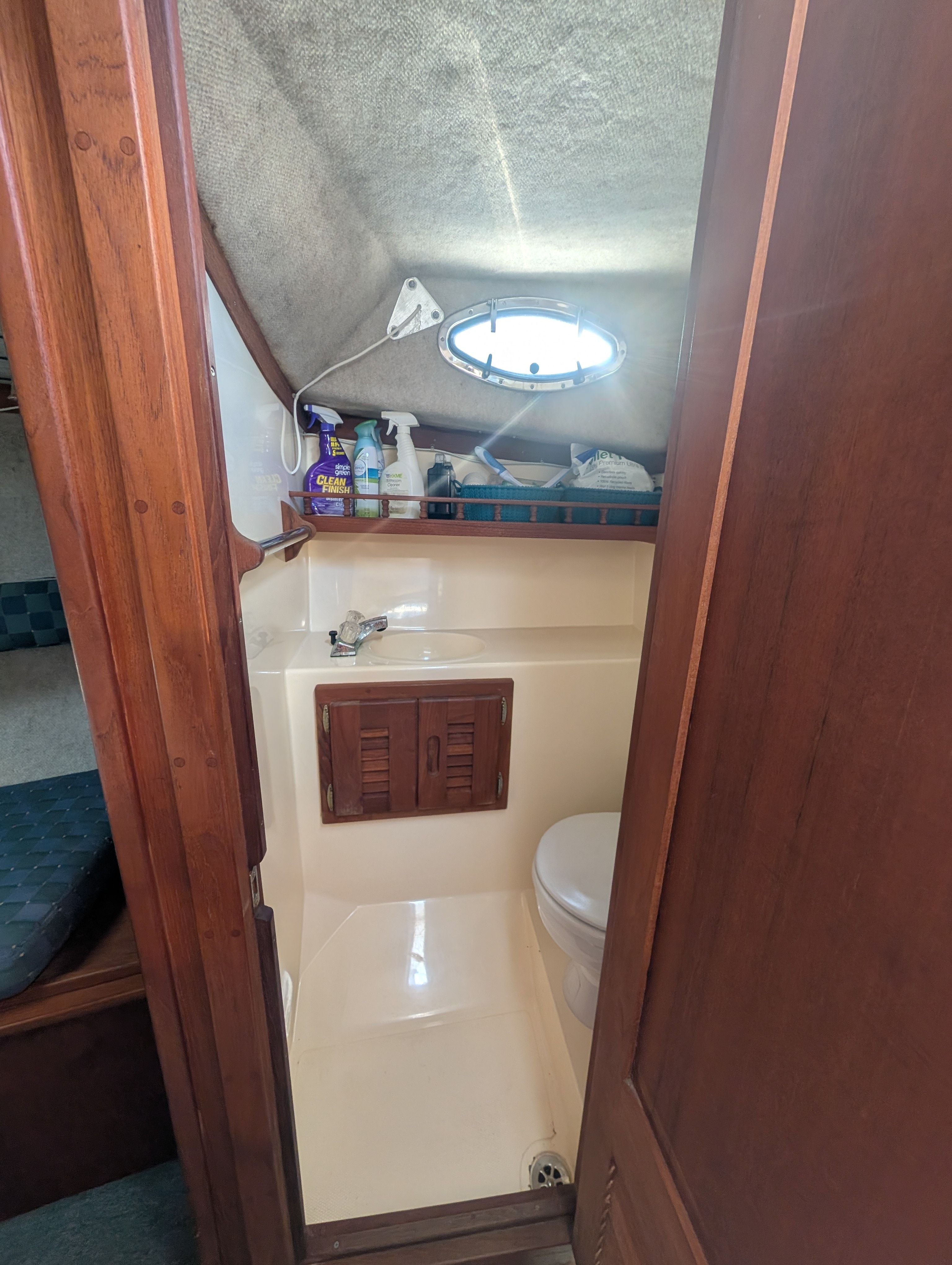 Small bathroom on a boat with toilet, sink, and cleaning supplies.