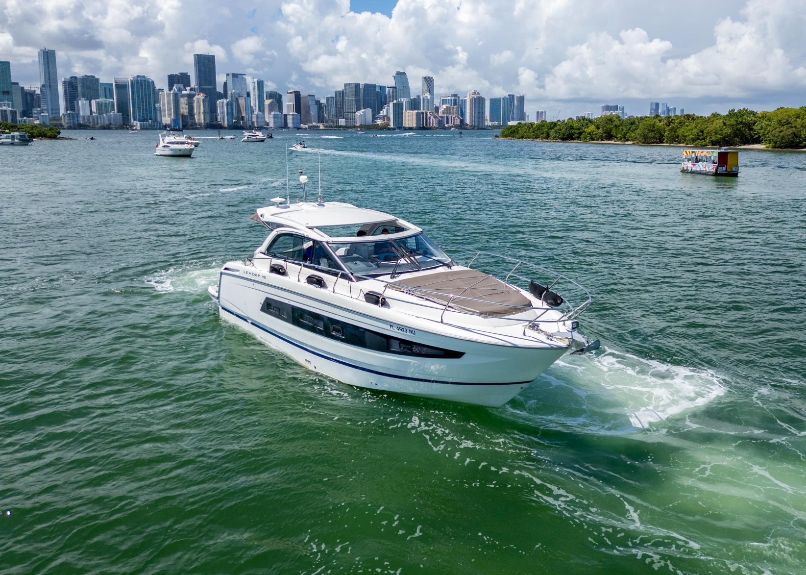 2019 Jeanneau Leader 40 yacht cruising near city skyline and lush greenery.