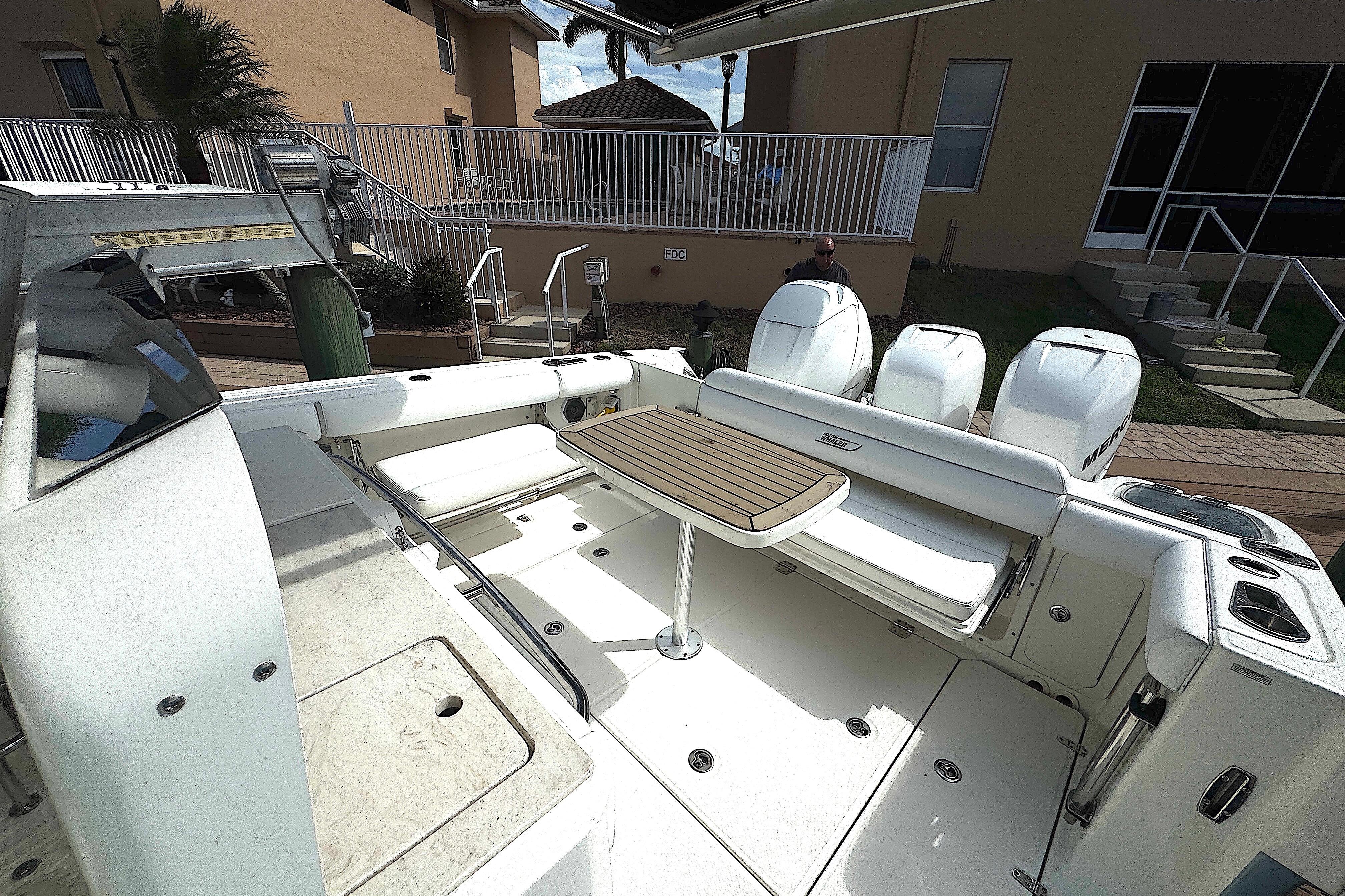 2014 Boston Whaler 350 Outrage boat interior with  side and rear seating with table, docked near a house.