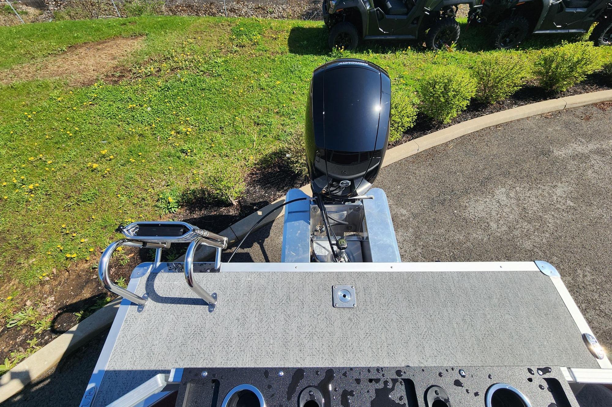 2026 Sun Tracker Fishin' Barge 22 DLX with outboard motor and ladder, parked on grass.