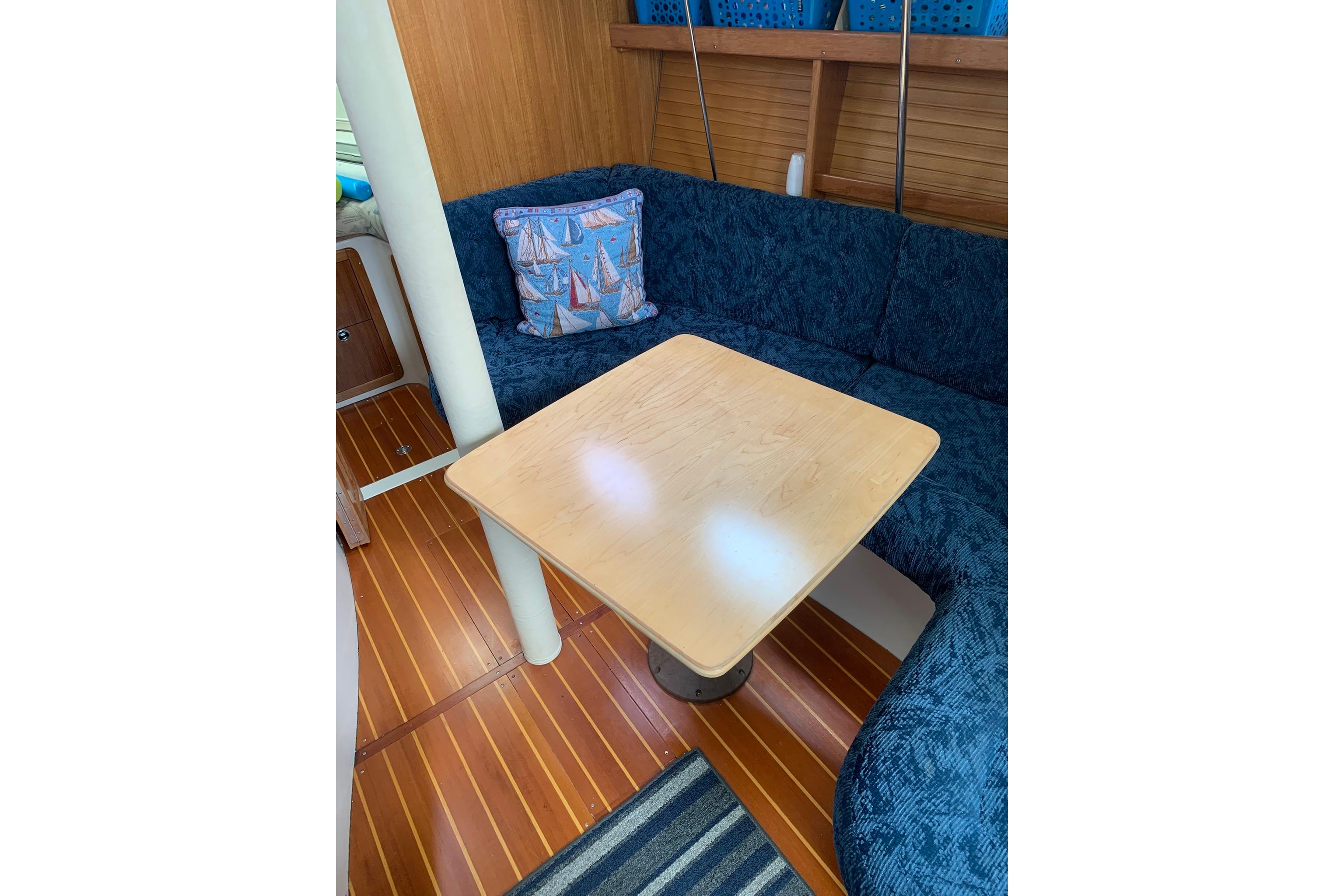 Cozy interior of 1998 Catalina 320 sailboat with blue seating and wooden table.
